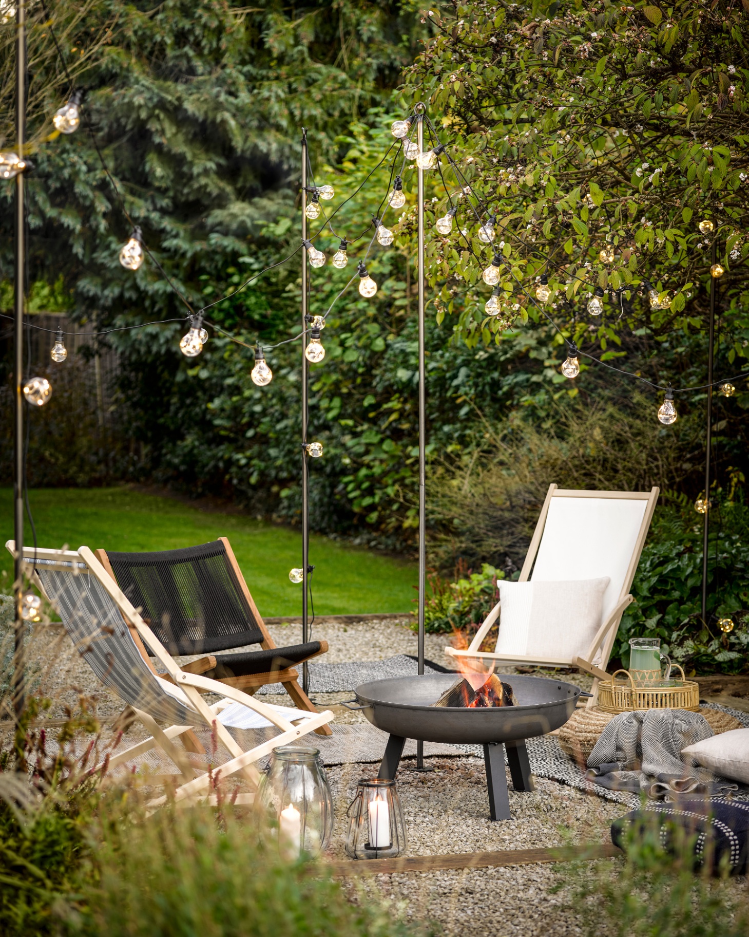 outdoor seating area with deck chairs surrounding a firepit with festoon lights overhead