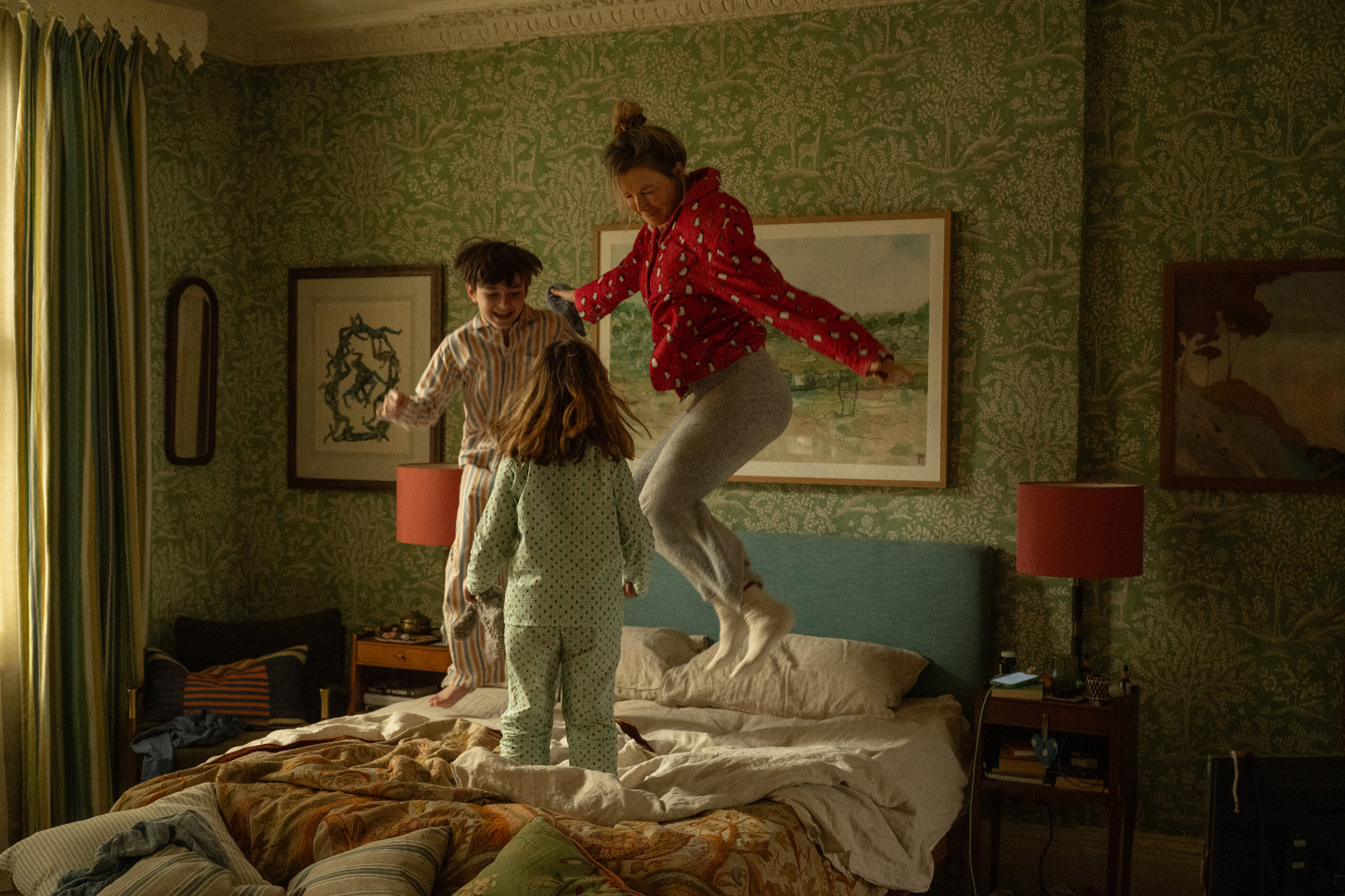 bridget jones and her children jumping on a bed with green botanical wallpaper on the walls