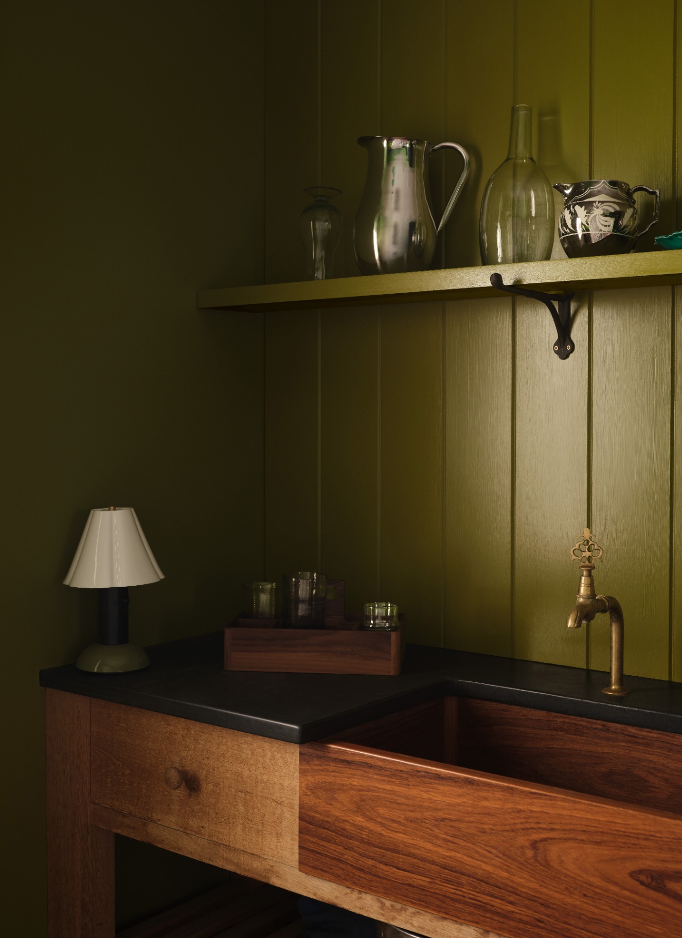 a utility room corner with tongue adn groove panelled walls and an open shelf drenched in olive green and a wooden sink area