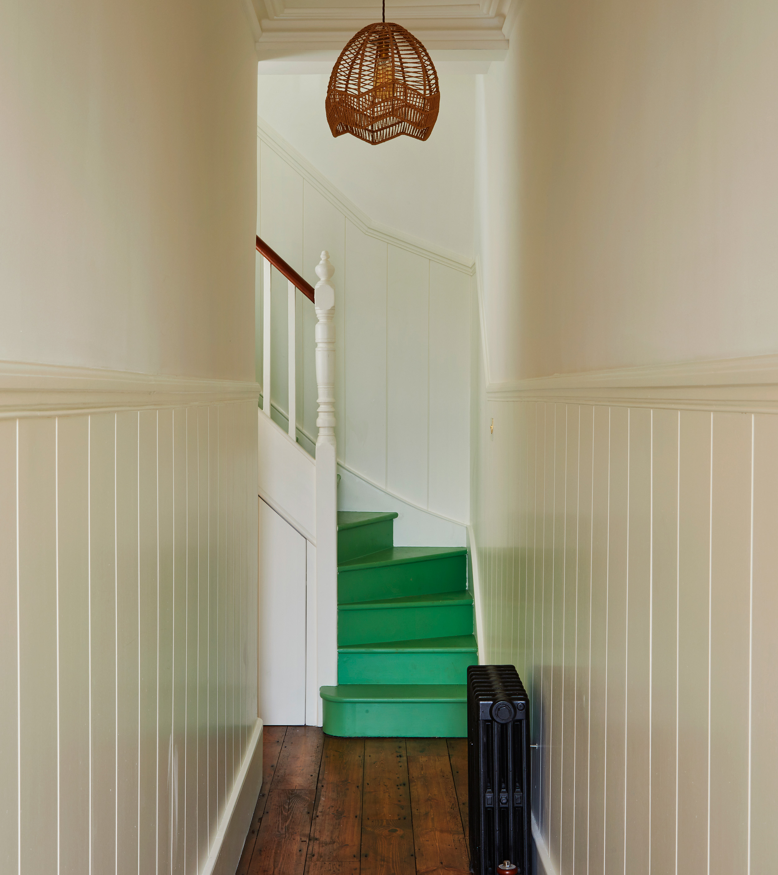 a white narrow hallway with bright green painted stairs
