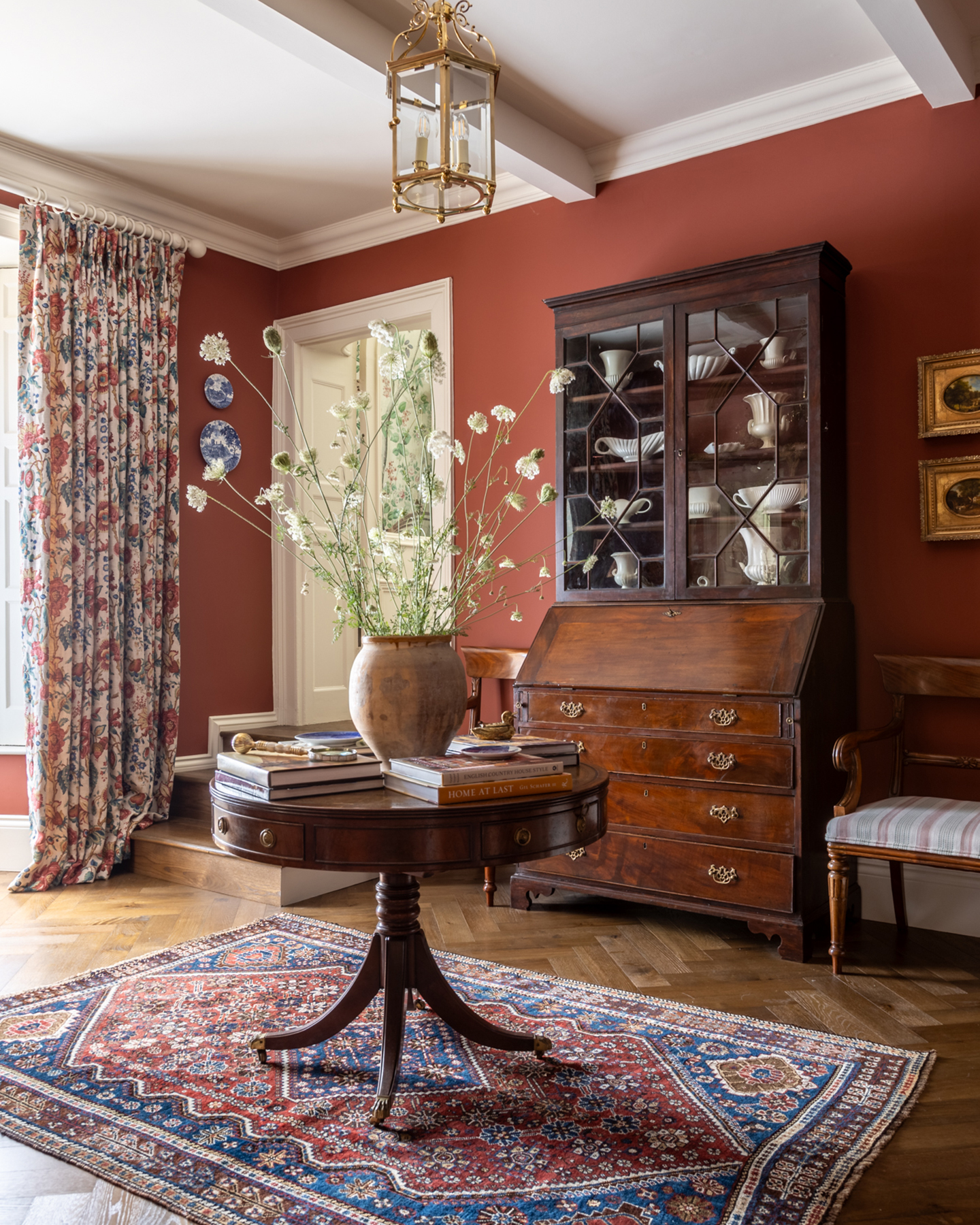 a hallway with red walls, a large dark wood antique dresser, a circle dark wood table in the centre with a blue and red persian rug underneath