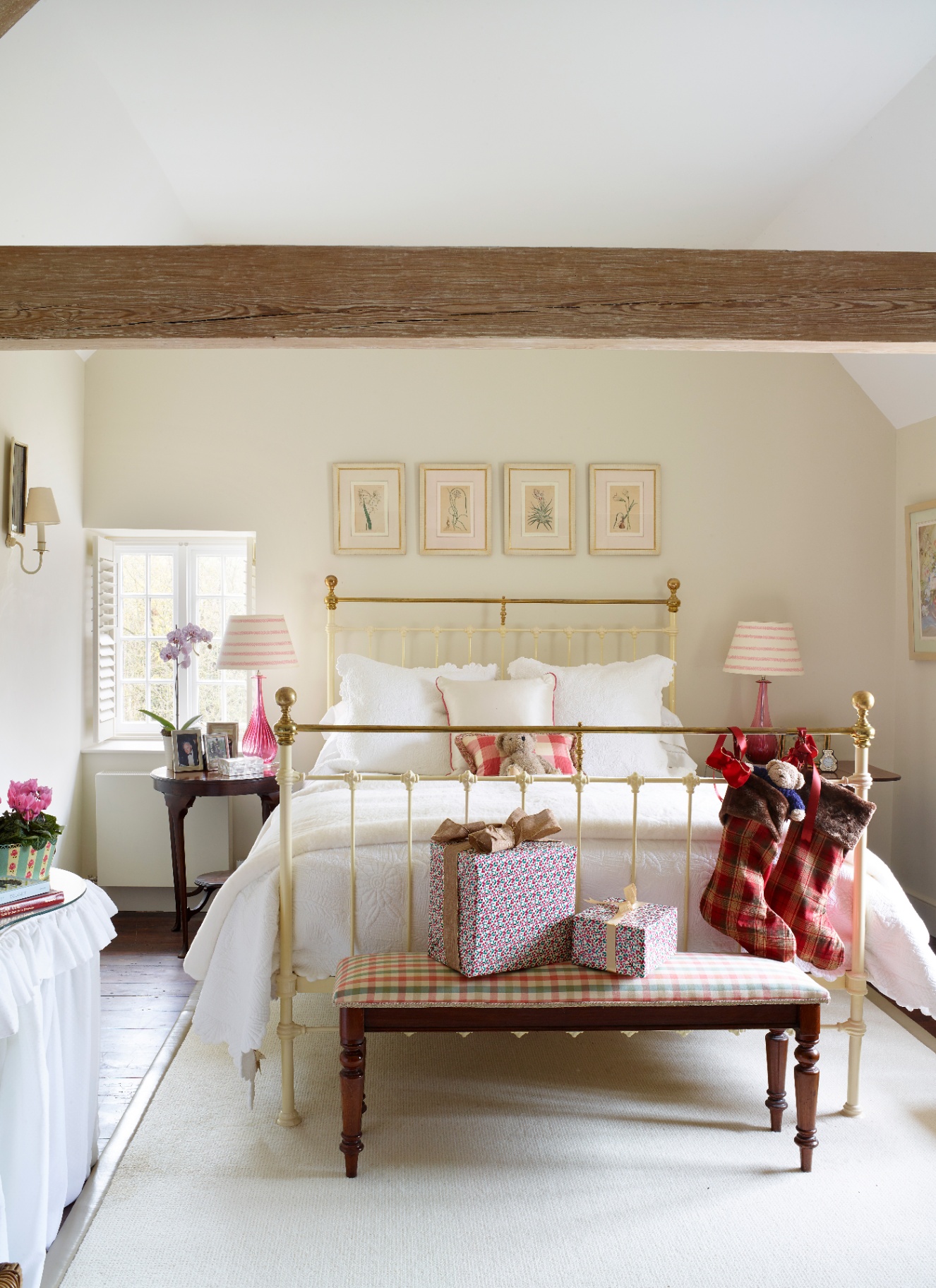 A bright guest bedroom featuring a vintage brass bed dressed with tartan stockings and wrapped gifts at the foot.