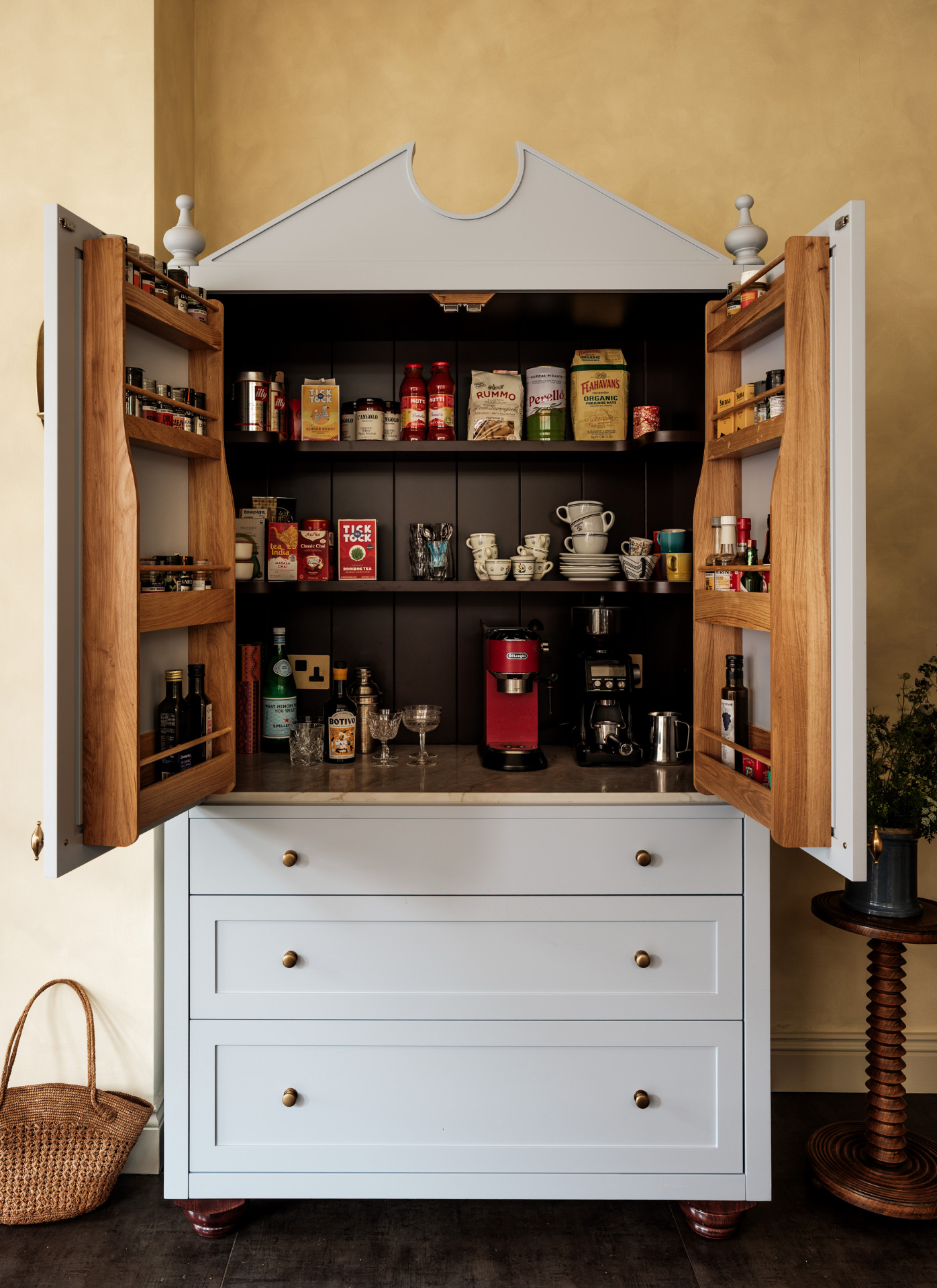 Period-style light blue dresser cabinet with open double doors revealing a dark painted interior, fitted oak door spice racks, coffee machines on marble worktop, and tea shelves above drawers