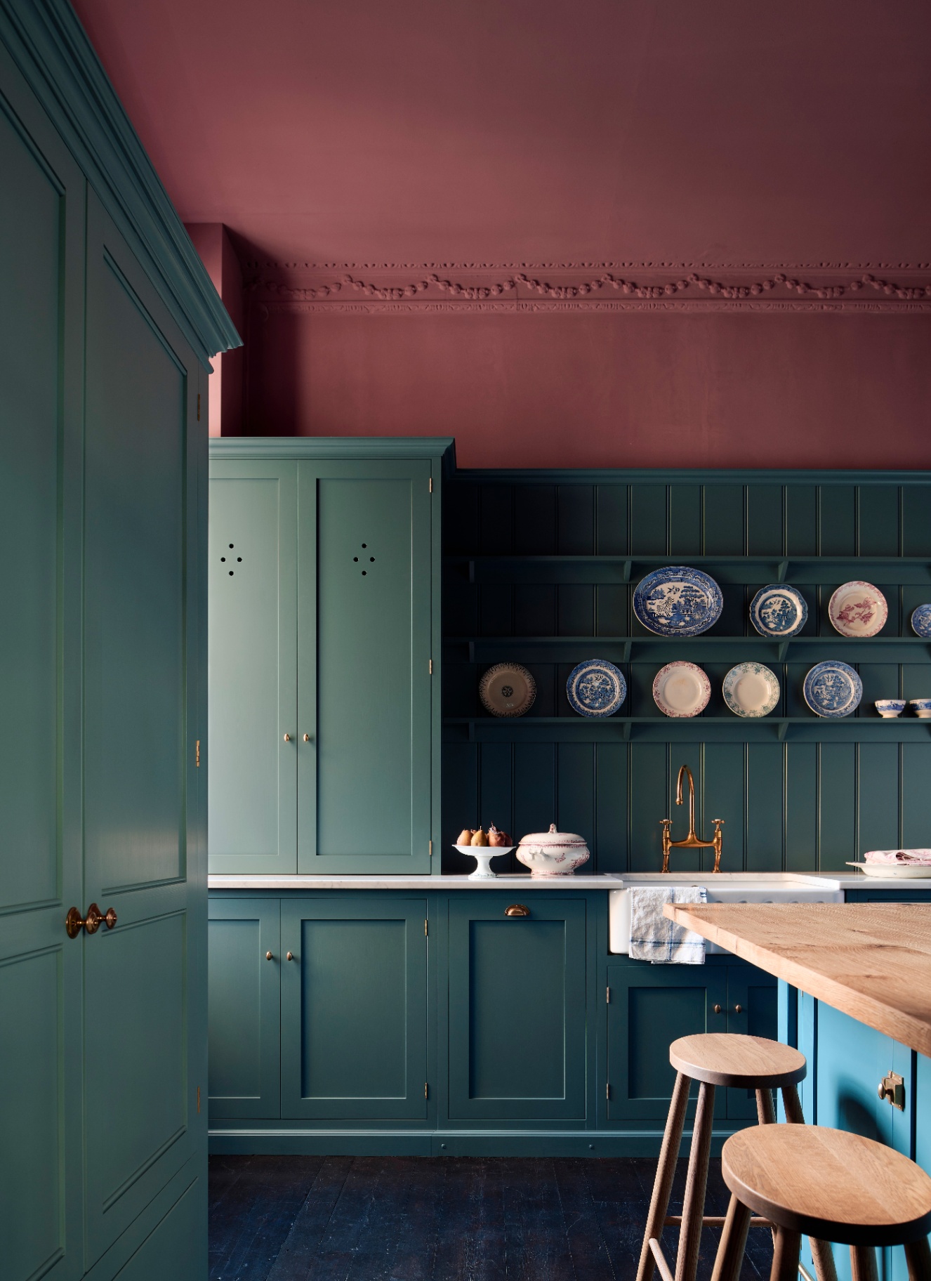 a kitchen with deep teal cabinets, dark wooden flooring and a red ceiling