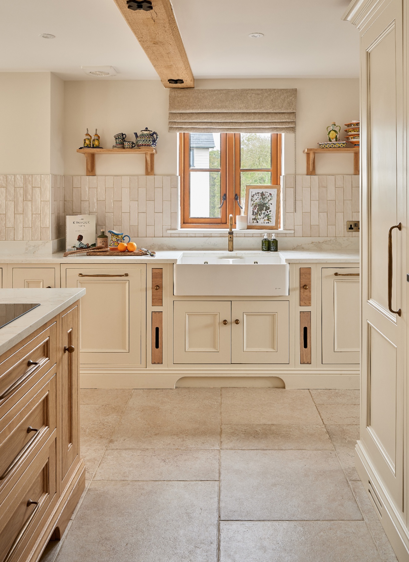 a neutral kitchen with a wooden island, pale stone floors, white cabinetry and white tiles