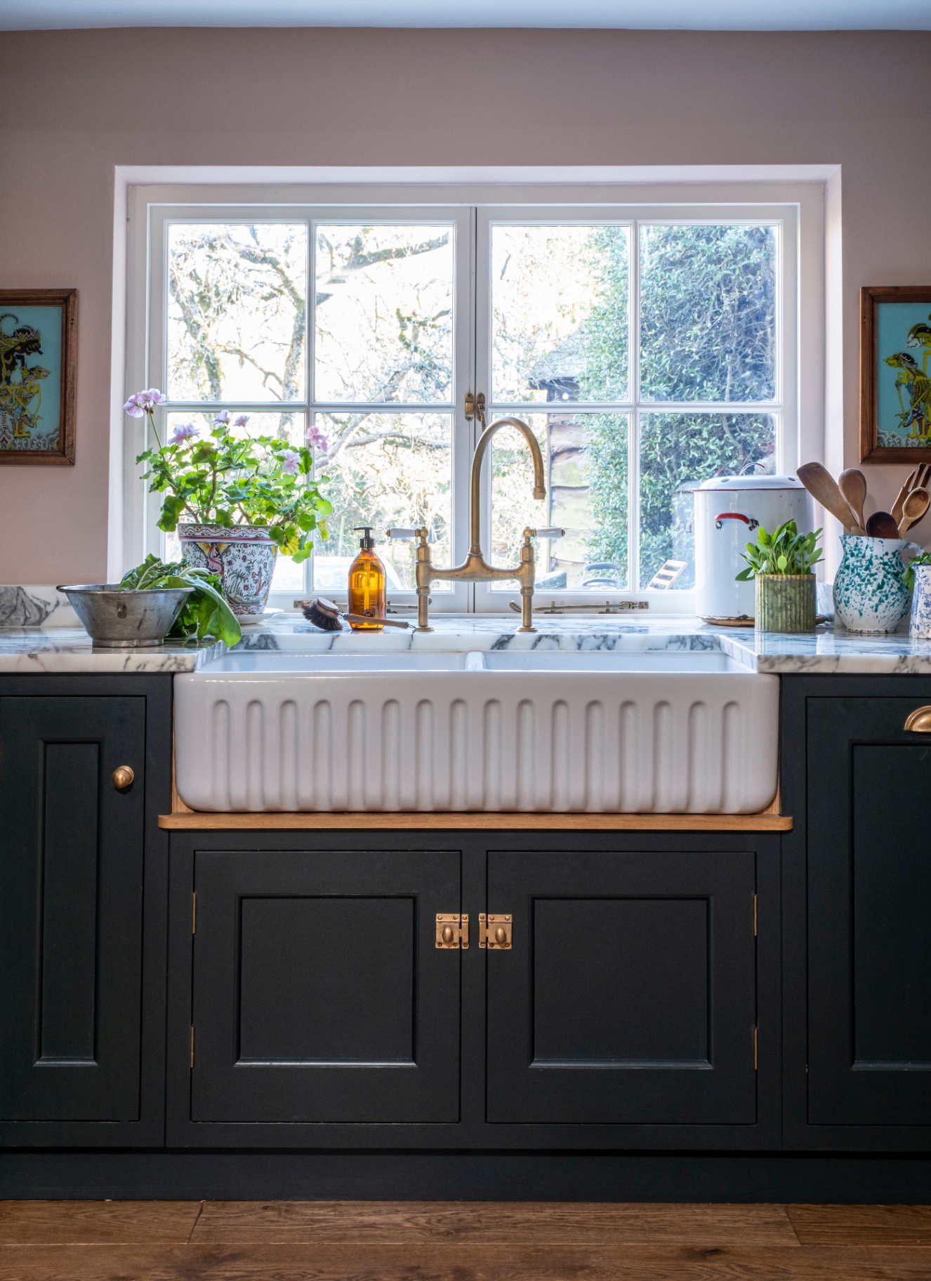 A KITCHEN WITH A DEEP BUTLERS SINK, DARK BLUE CABINETRY, MARBLE COUNTER TOPS AND PALE PINK WALLS