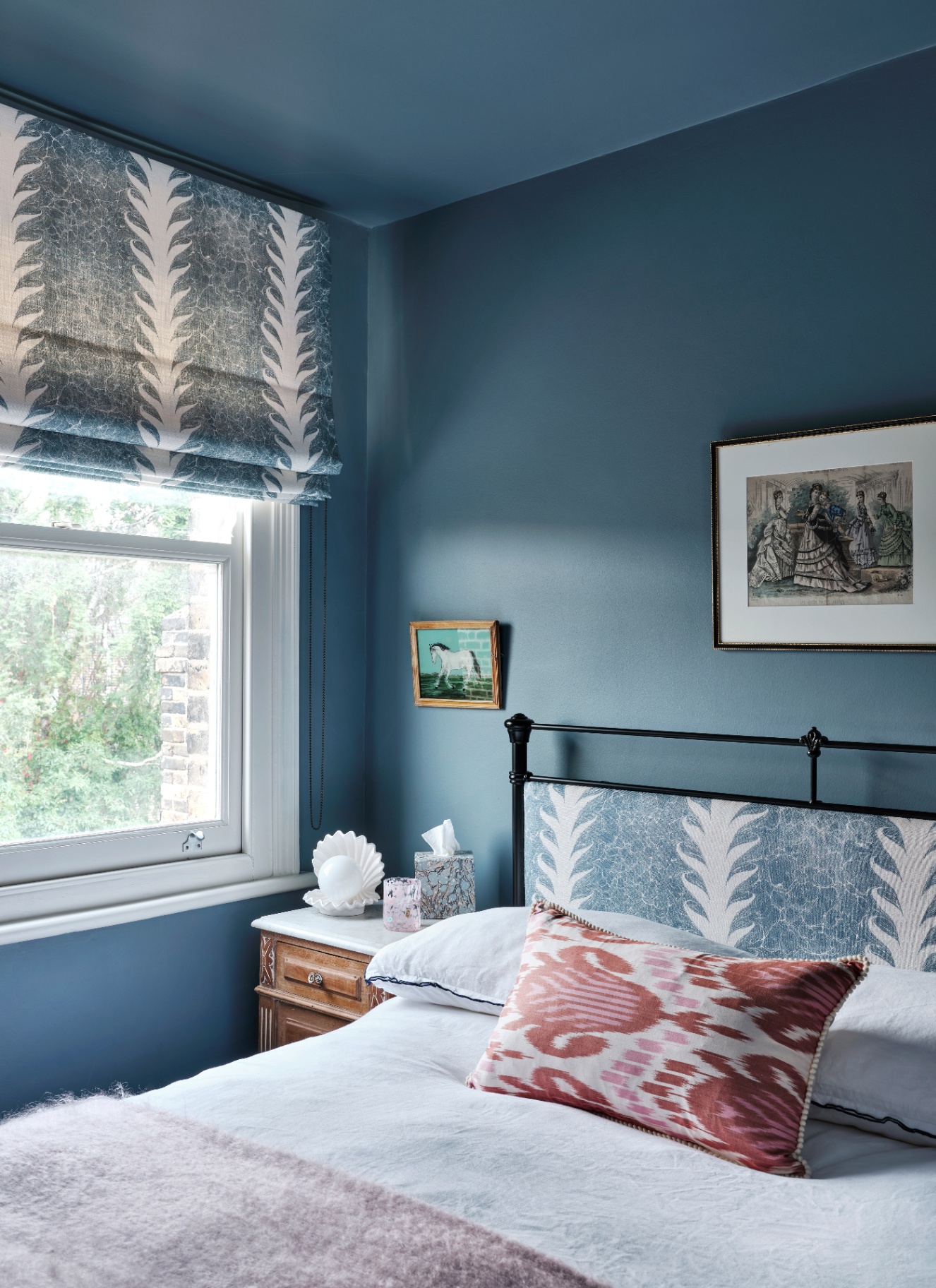 a bedroom with blue walls and ceiling, a bed with white bedding and a red and white patterned cushion and a bedside table with a clam shape light