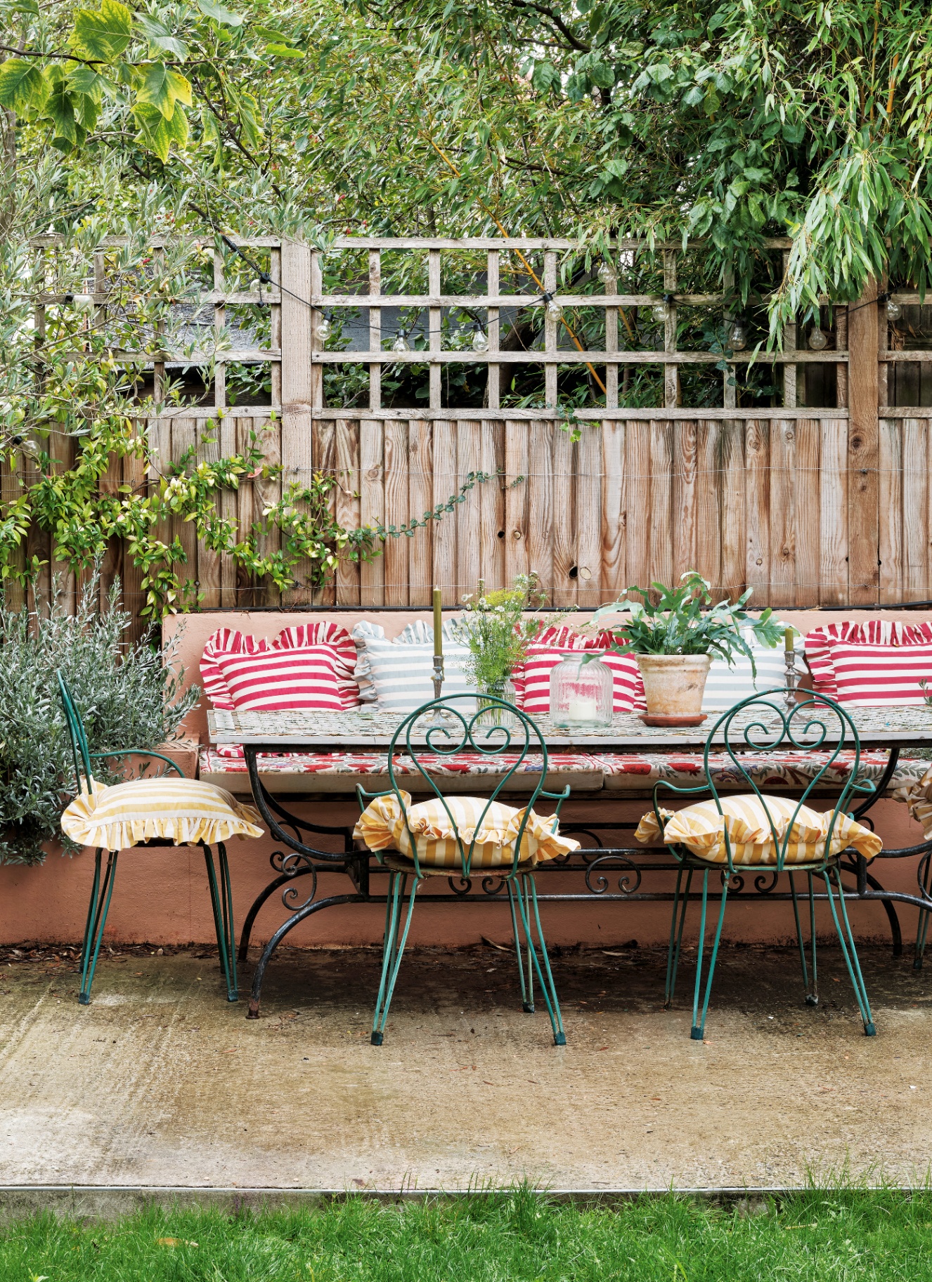 an outdoor patio area with a long green iron table and chairs with multicolour striped cushions