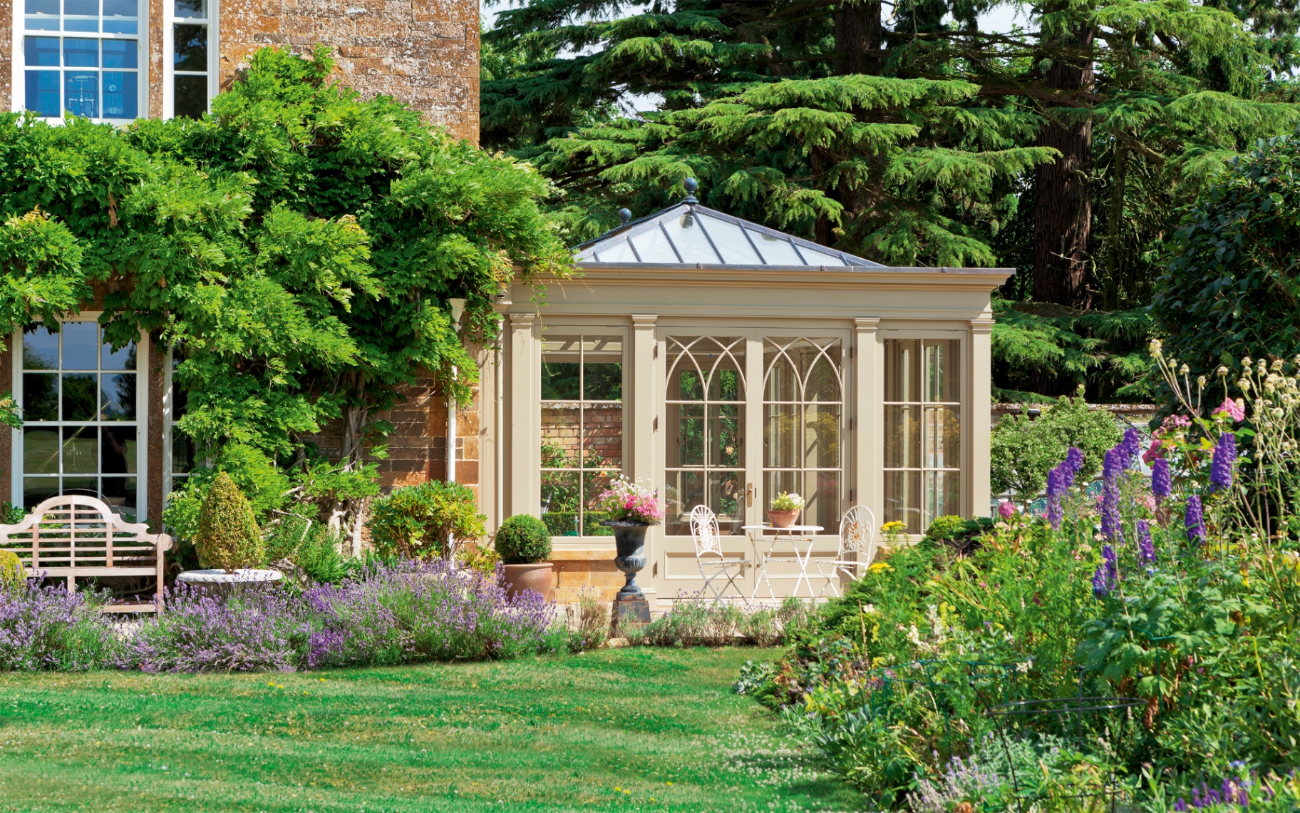 a beige garden room seen from the outsode surrounded by summer greenery and flowers