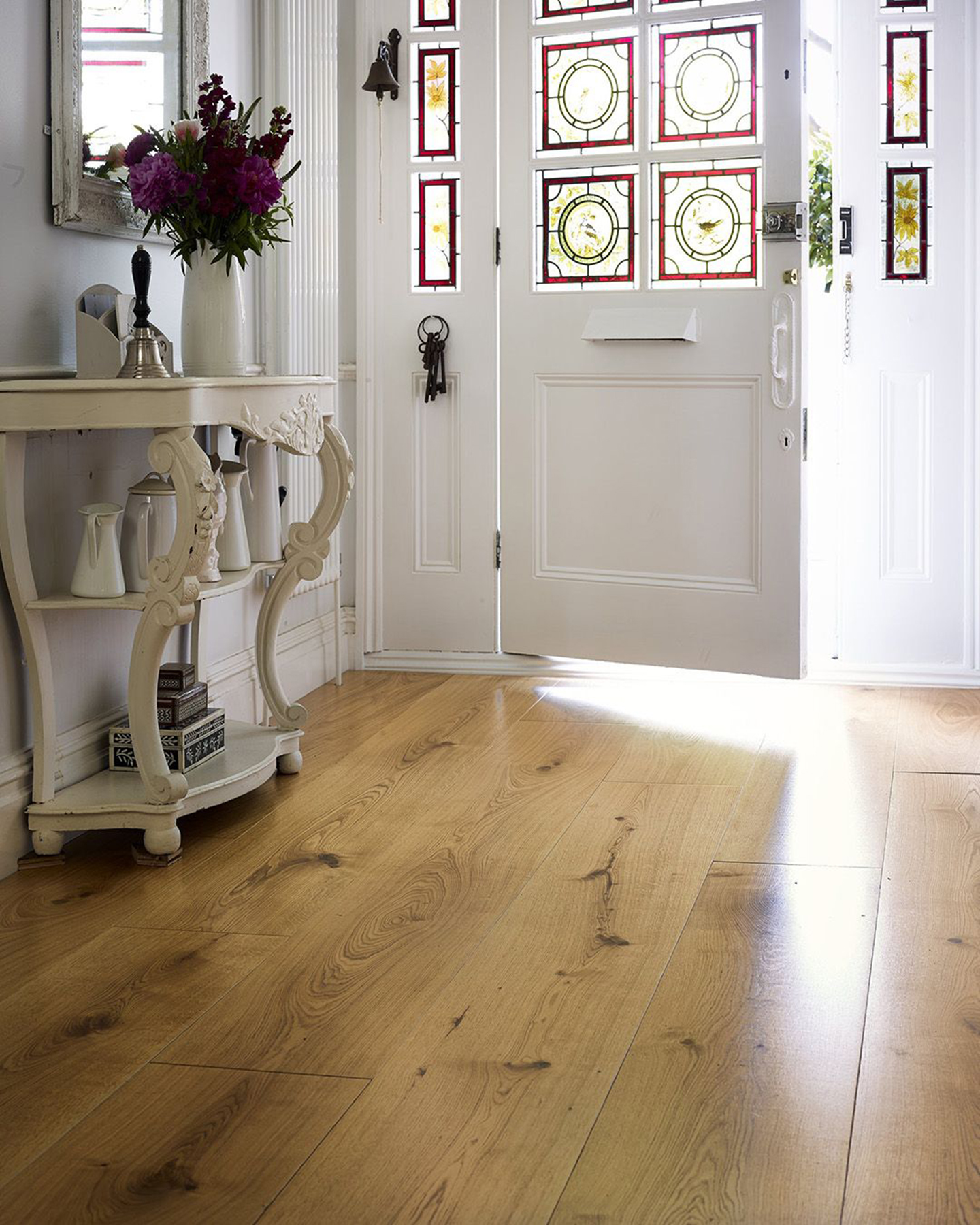 a dining room with wooden parquet flooring, a dining table with 5 wooden chairs and a vase filled with flowers, a large curved window, a fireplace to the left and a white built in cupboard next to it