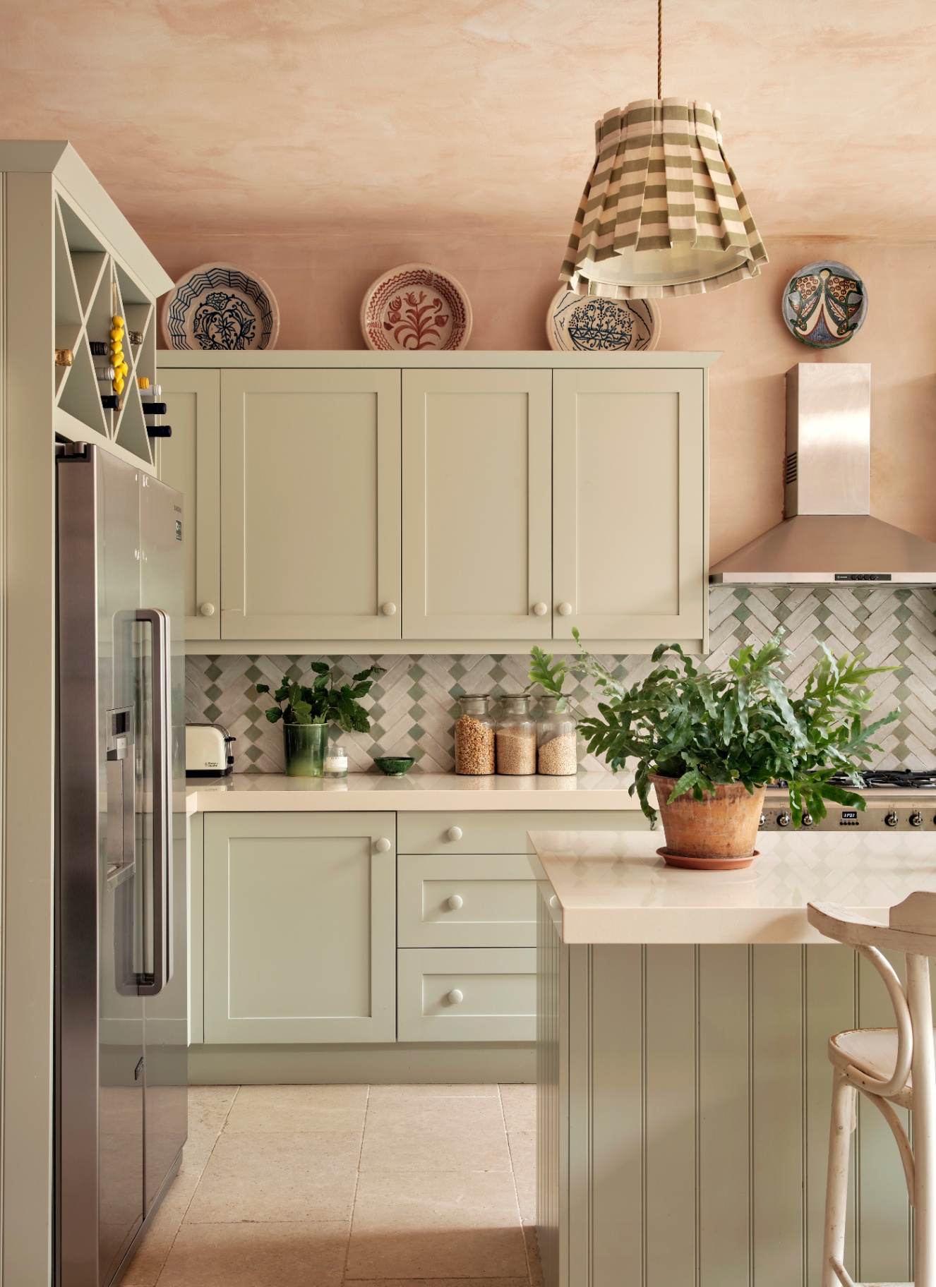 a kitchen with pale green cabinetry, a silver double fridge and a green and white stripe pleated pendant light above the kitchen island