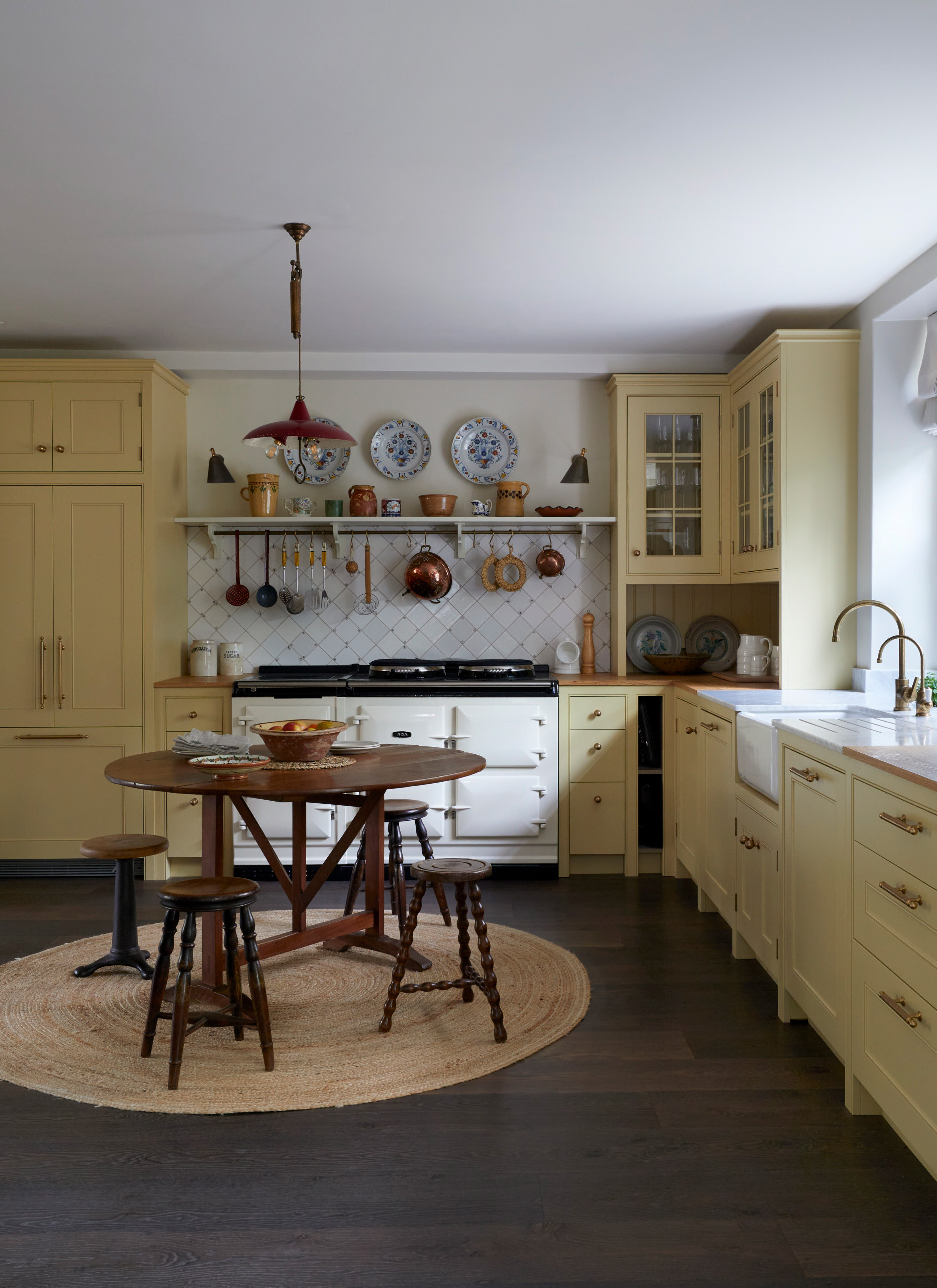 a kitchen wil pale yellow cabinetry, sa white range cooker and a dark wooden round dining table with matching stools and a round jute rug under it