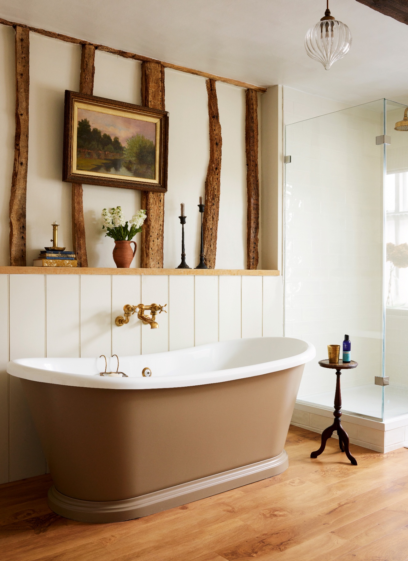 a bathroom with a beige freestanding bath tub and a recessed shelf with white walls and exposed beams
