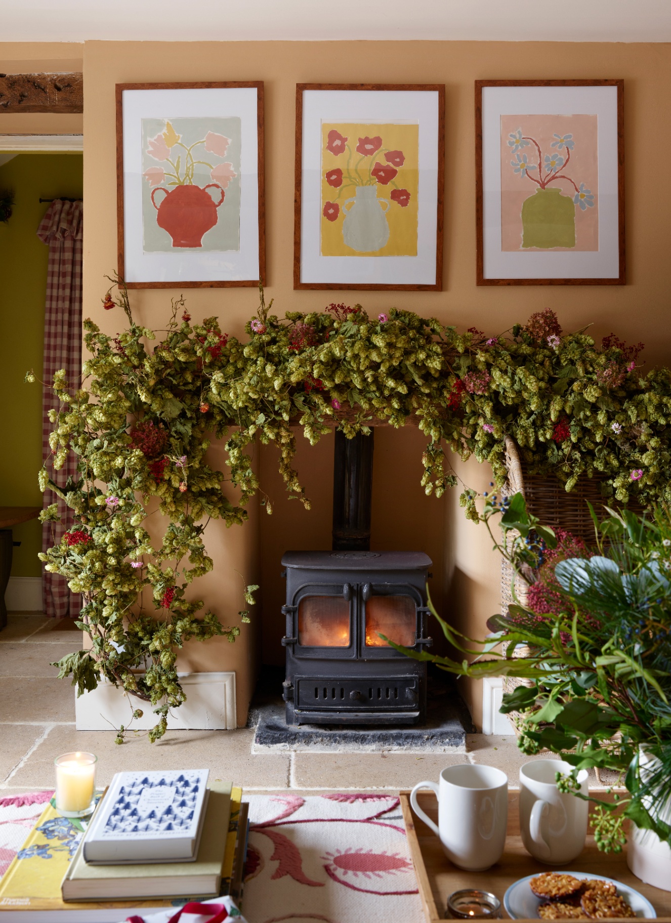 A rustic fireplace and wood-burning stove framed by a heavy, sweeping garland of natural dried hops