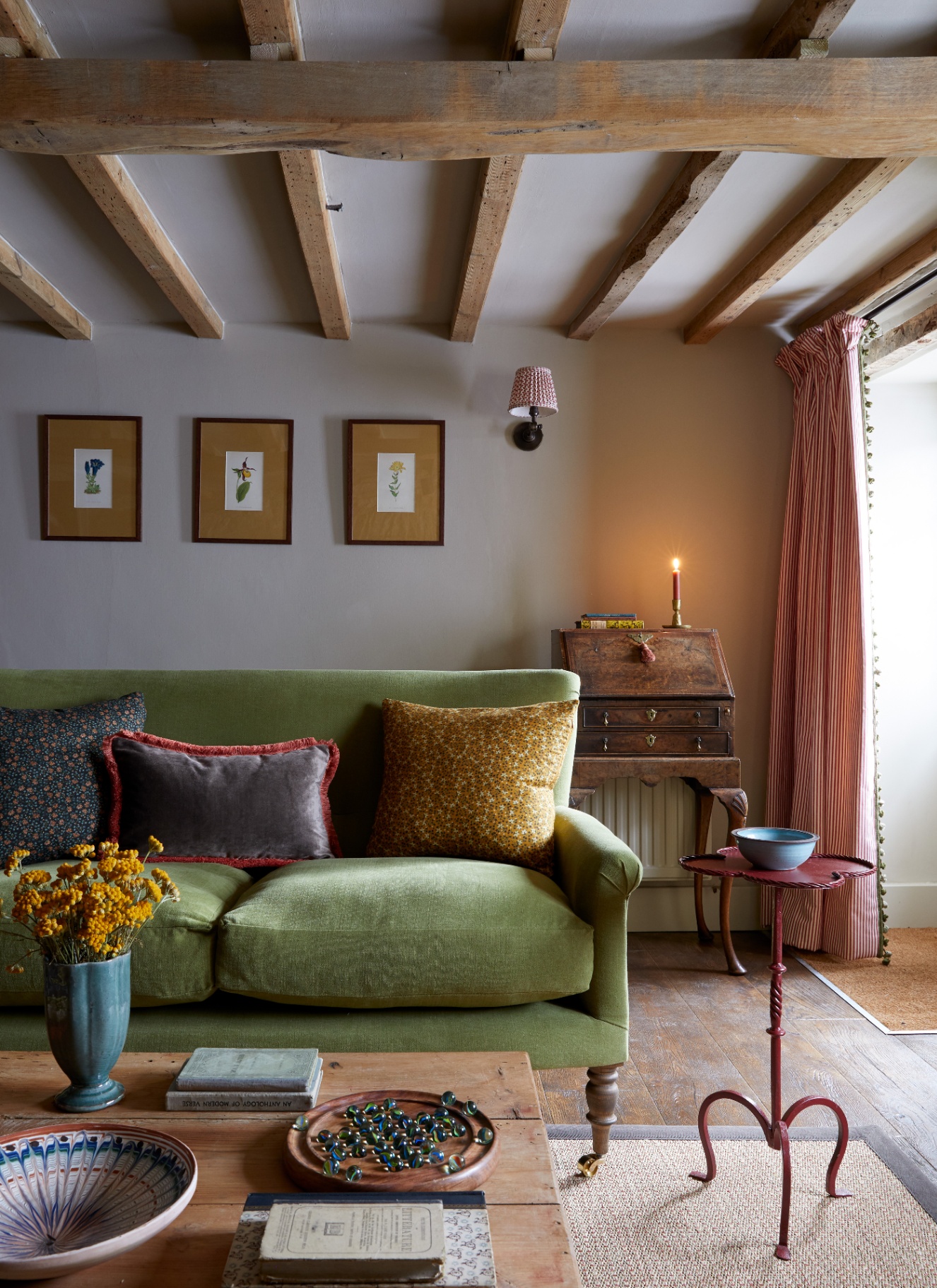 a cottage style living room with wooden beams, an olive green sofa, a wooden coffee table and a small red iron side table