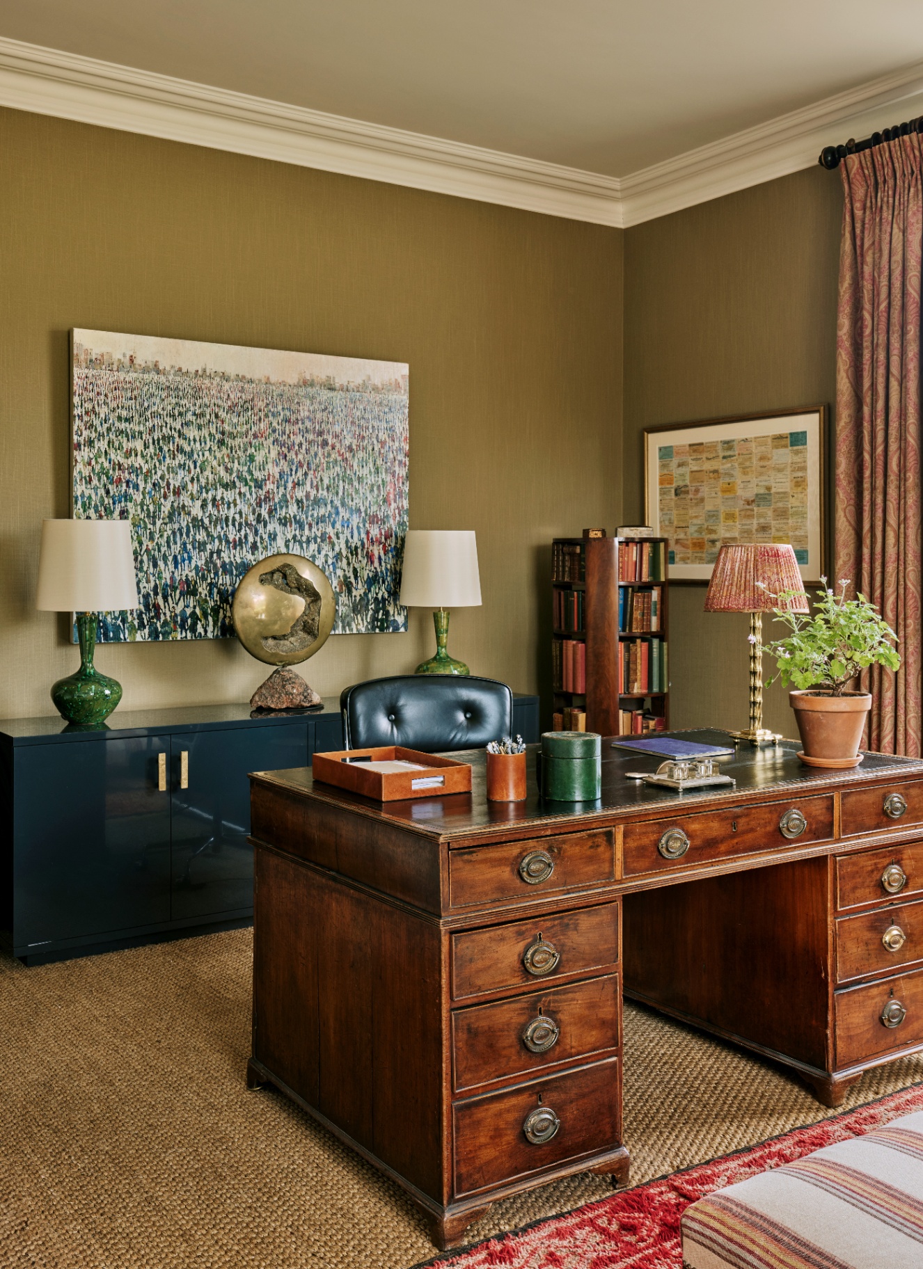 Traditional executive study with warm brown walls, a large antique mahogany pedestal desk, dark leather chair, jute rug, and floor-length patterned curtains