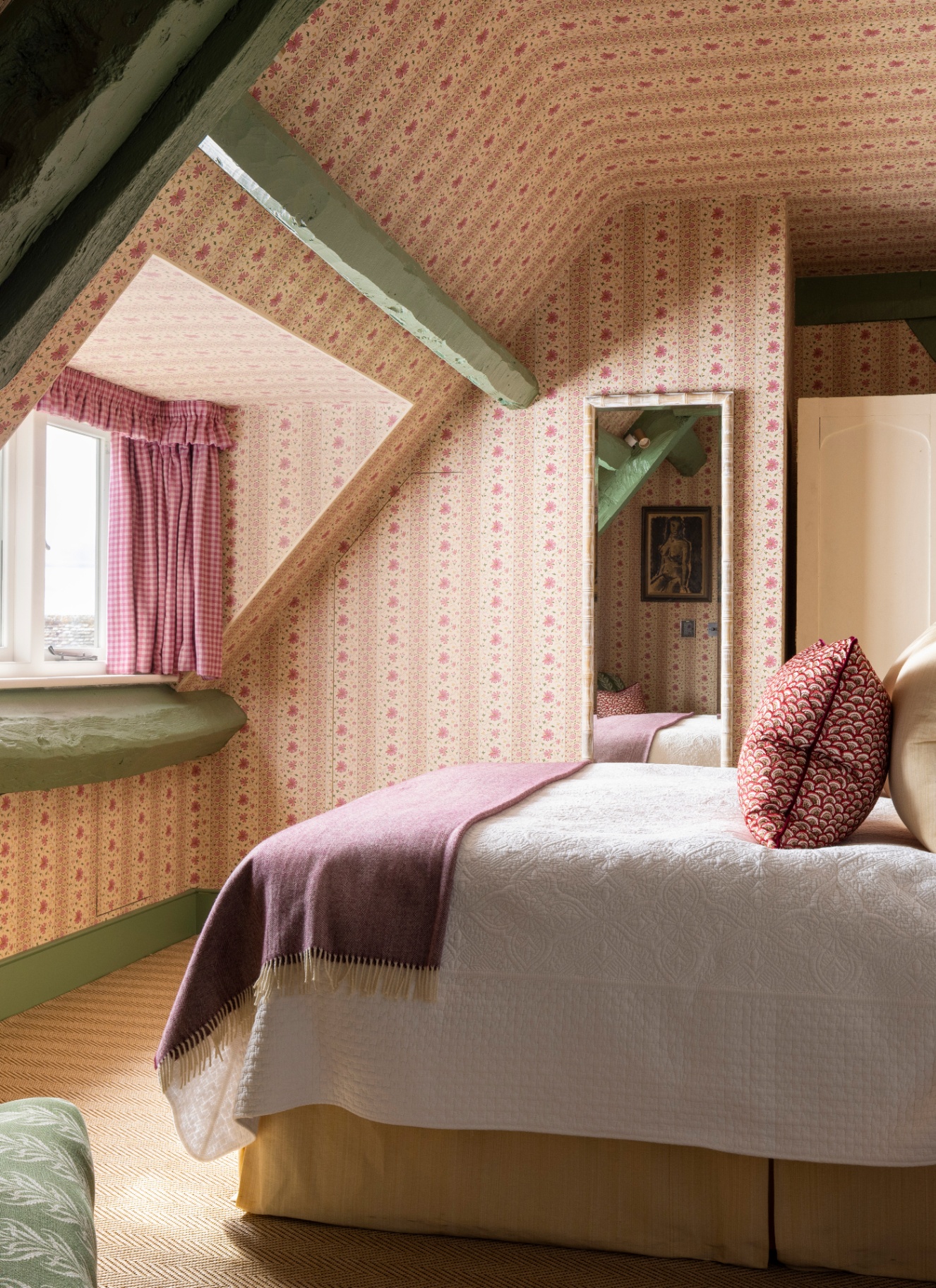 a bedroom with eaves ceiling wrapped in a pale pink floral wallpaper, pale green painted beams and a bed with white and pink bedding
