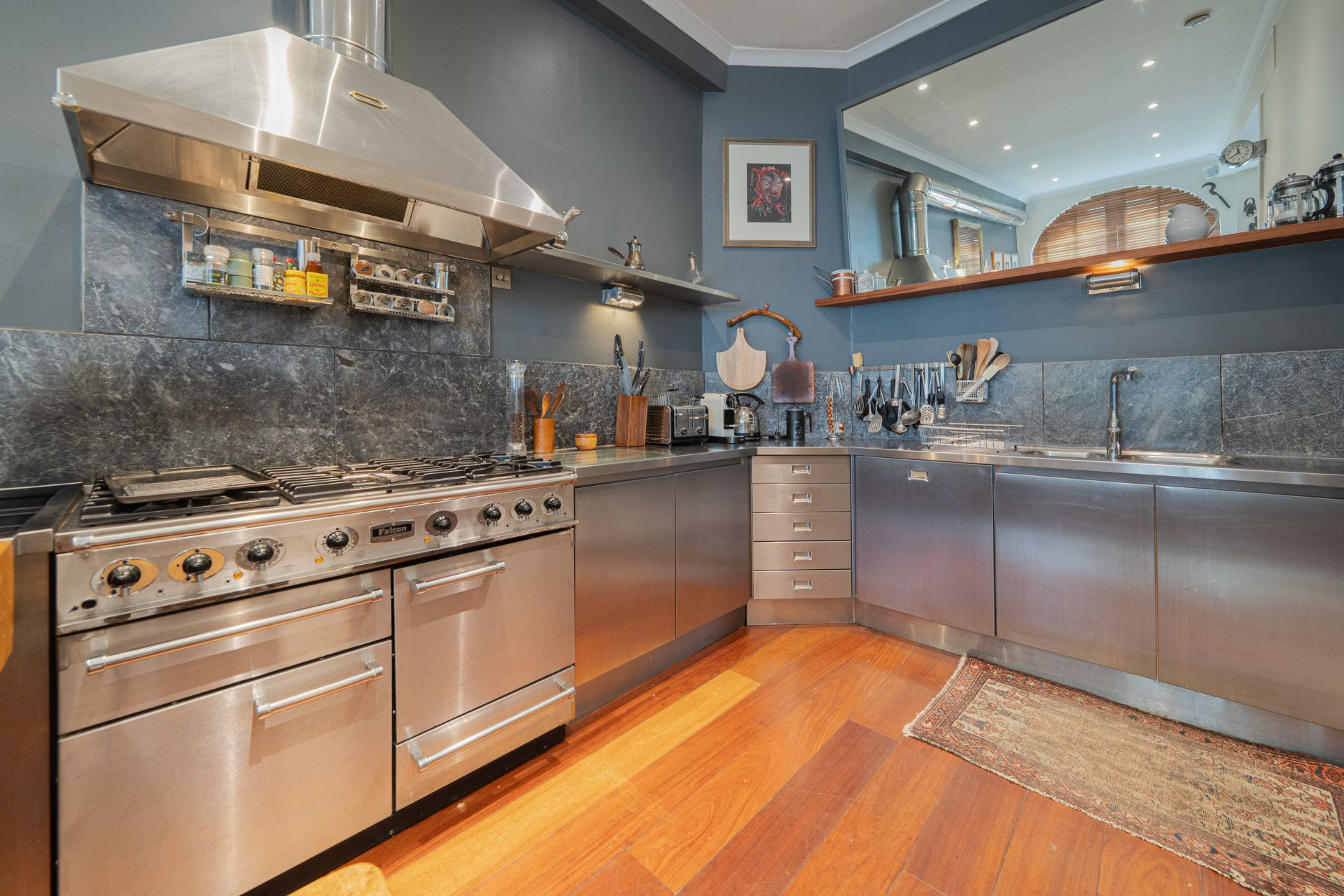 a kitchen with a large silver range cooker, silker cabinets, petrol blue walls and wooden floor