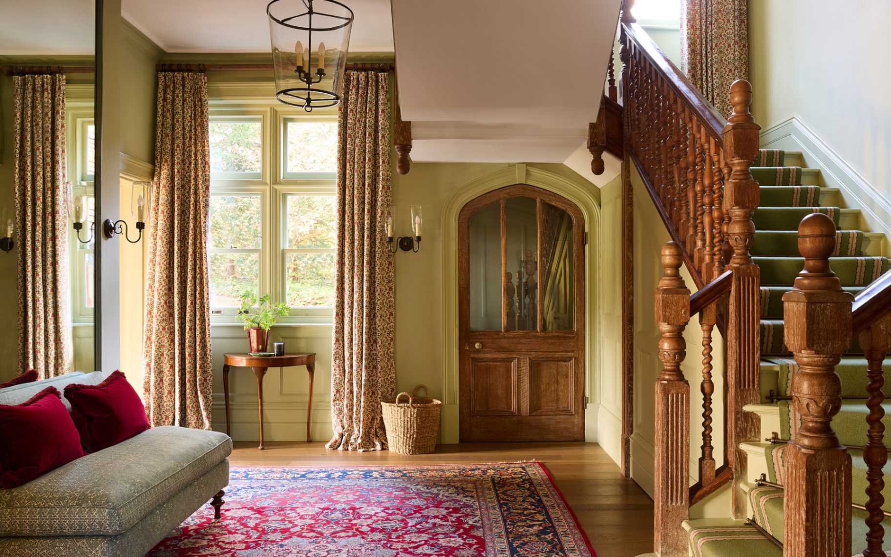 a grand hallway with green and white walls, a red patterned carpet and long neutral floral curtains