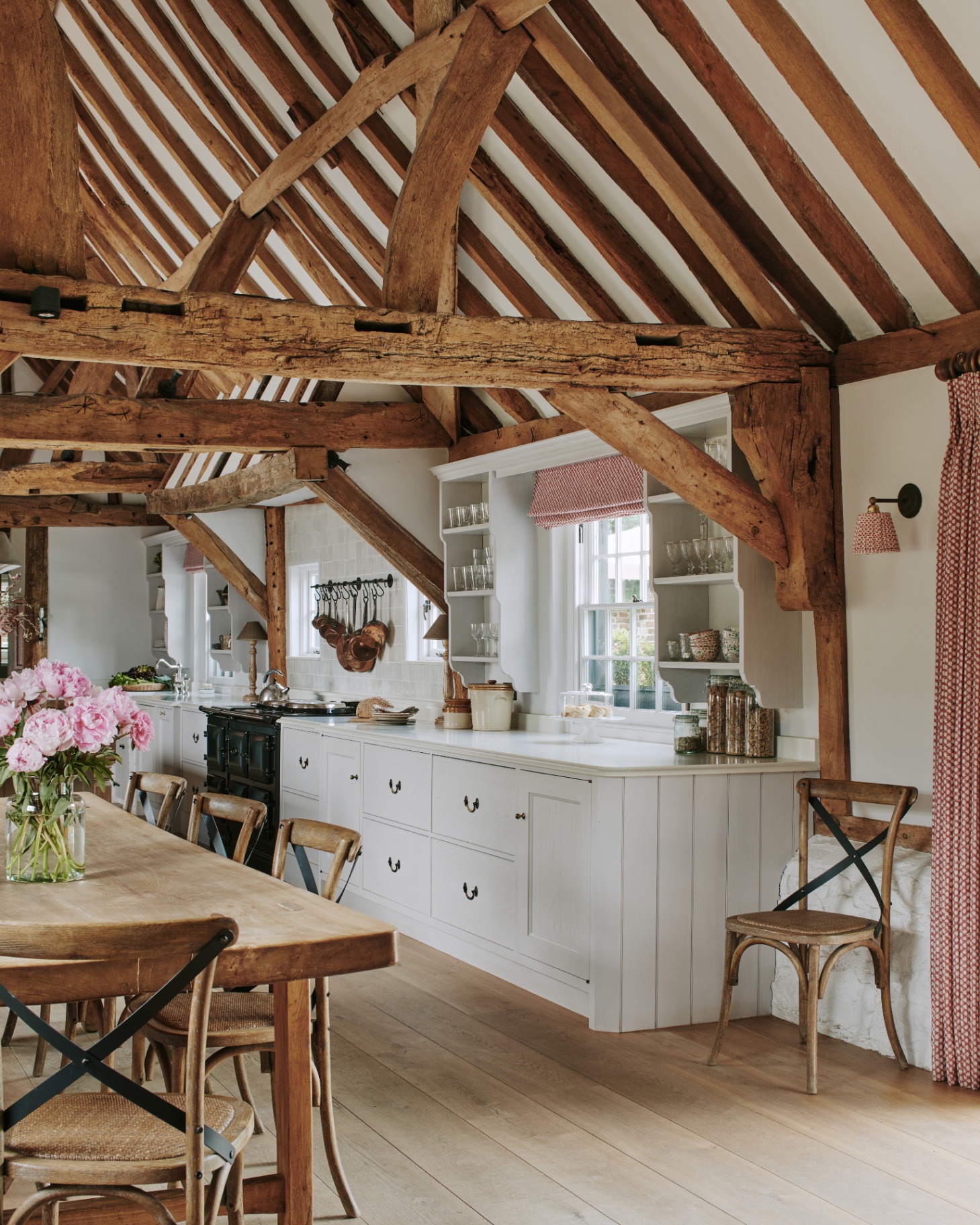 a kitchen with wooden exposed beams on the ceiling, a wooden dining table and chairs and white kitchen cabinetry