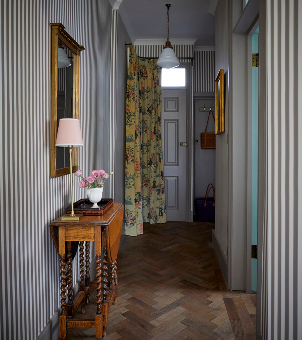 a narrow hallway with grey and white stripe walls, a yellow floral curtain in front of the front door, a dark oak console table with a wooden mirror above it