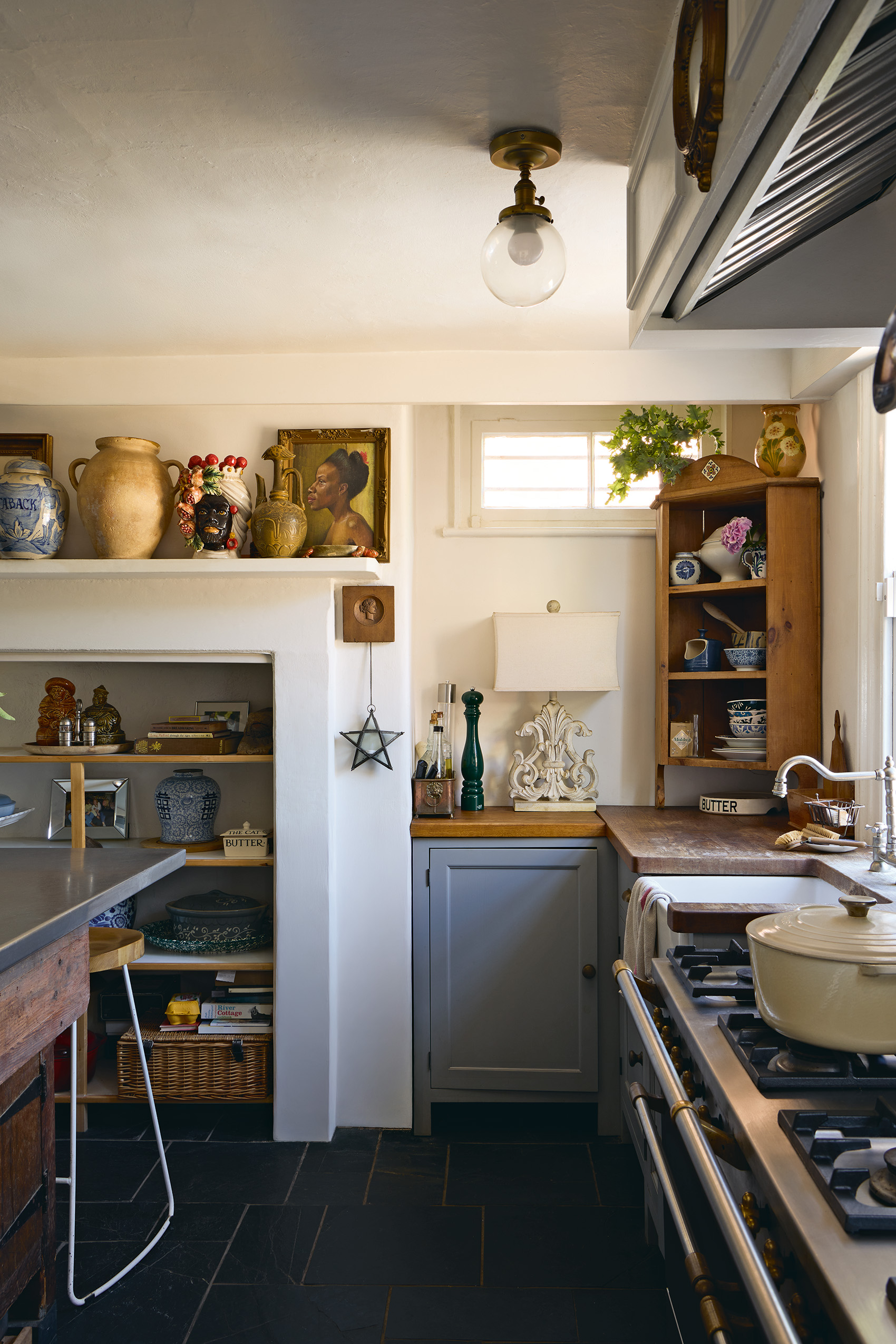 a kitchen with neutral walls, black floor tiles and grey cabinets with wooden worktops, vintage ceramics and accessories line a mantel and corner cabinet
