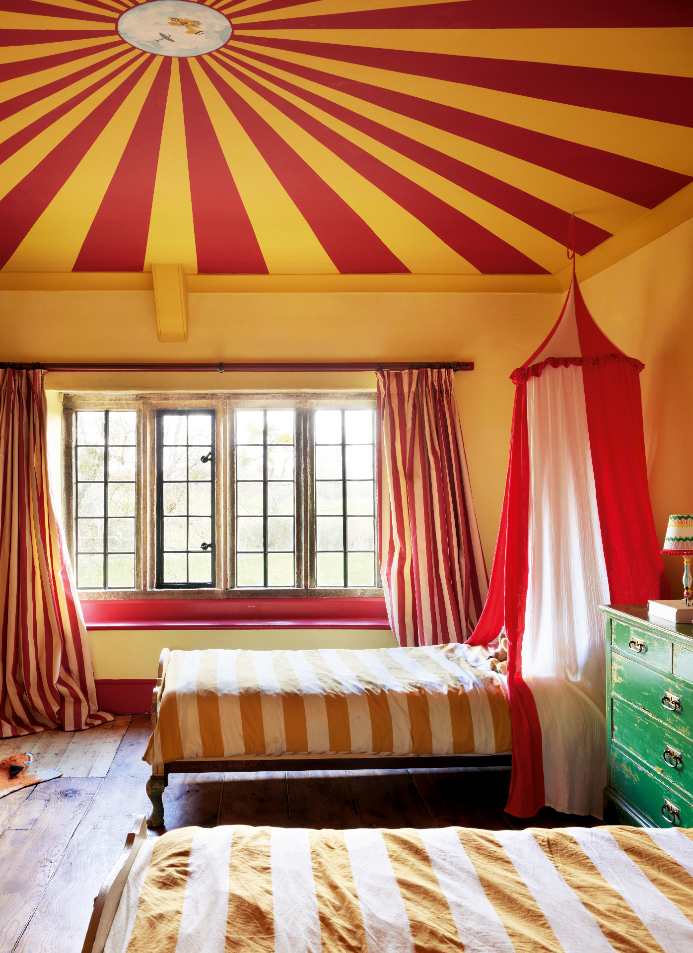 a childrens bedroom with a yellow and red circus stripe ceiling and two single beds with a red and white canopy