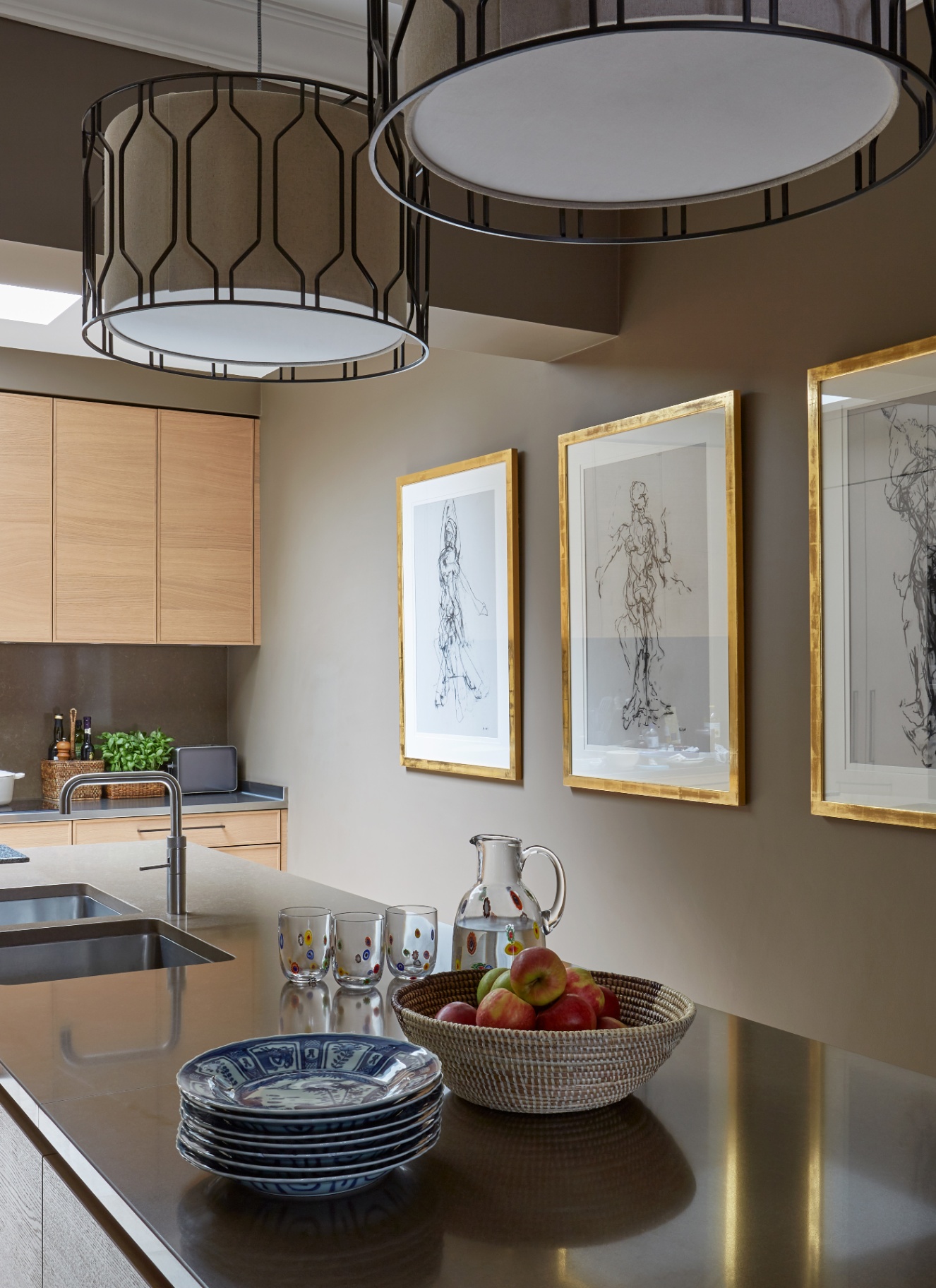 a narrow kitchen with brown walls, two large drum lampshades and gold framed prints on the wall