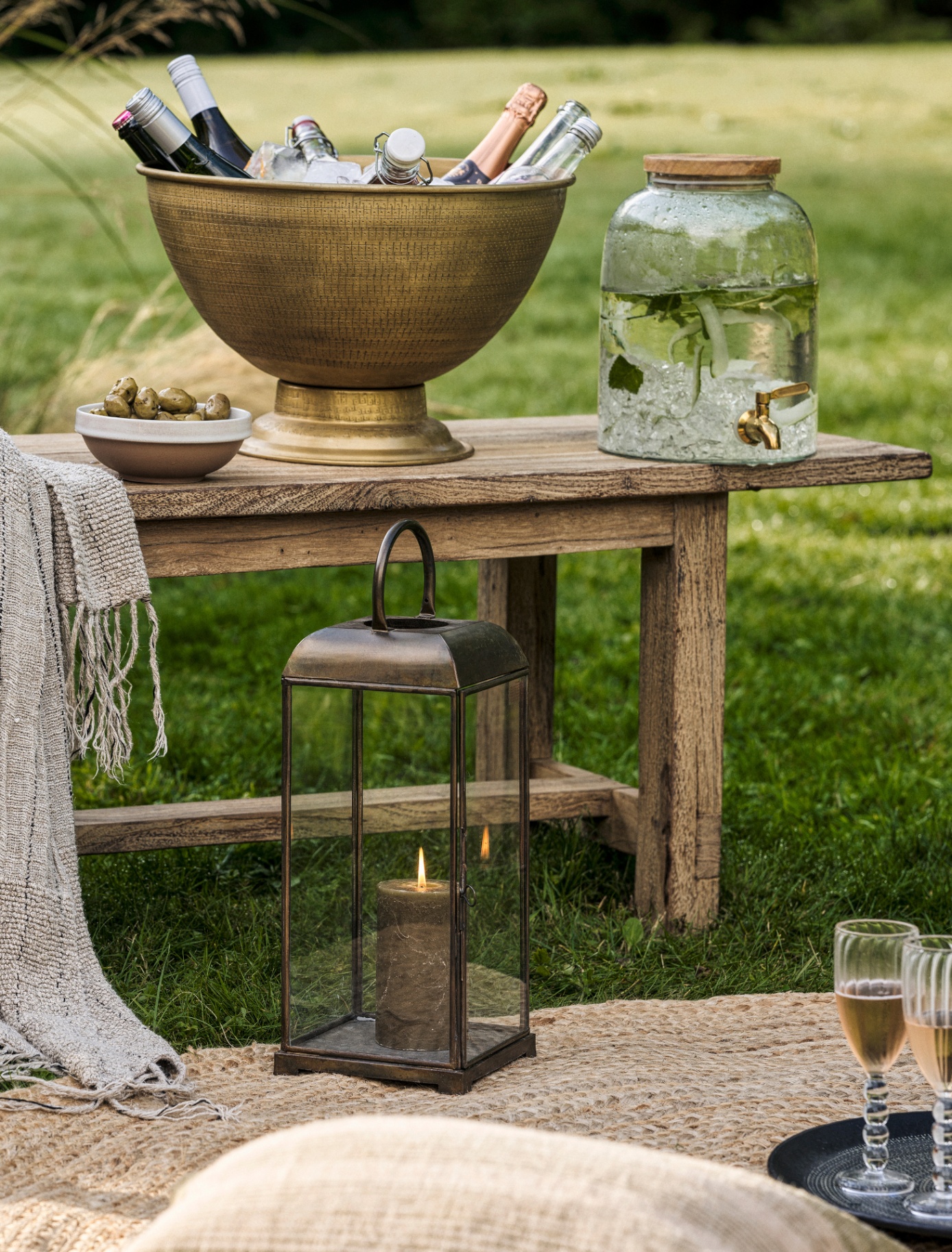 A WOODEN OUTDOOR BENCH with agold champagne bucket on top filled with champagne bottles