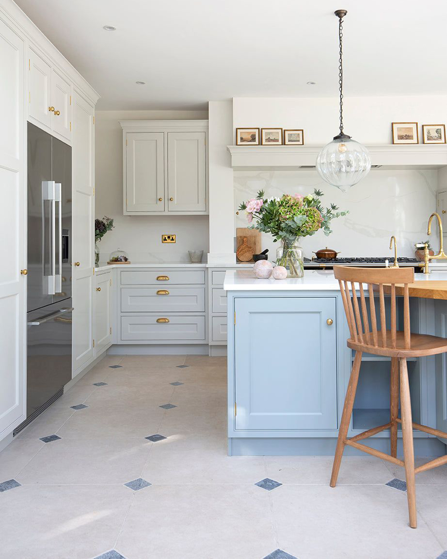 a kitchen with white and grey limestone flooring, white kitchen cabinets and a pale blue kitchen island with a glass pendant light above it