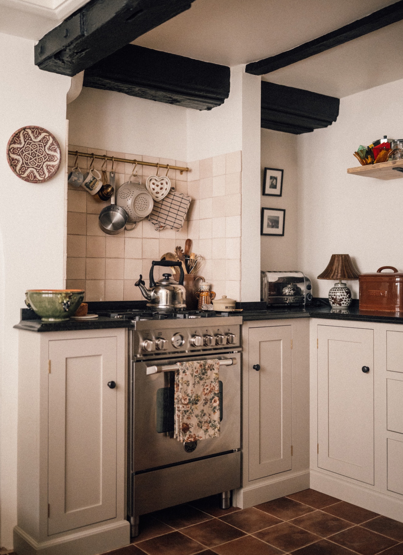 a country kitchen with a silver cooker, white walls and cabinets, black wooden beams and pots and pans hanging above the cooker