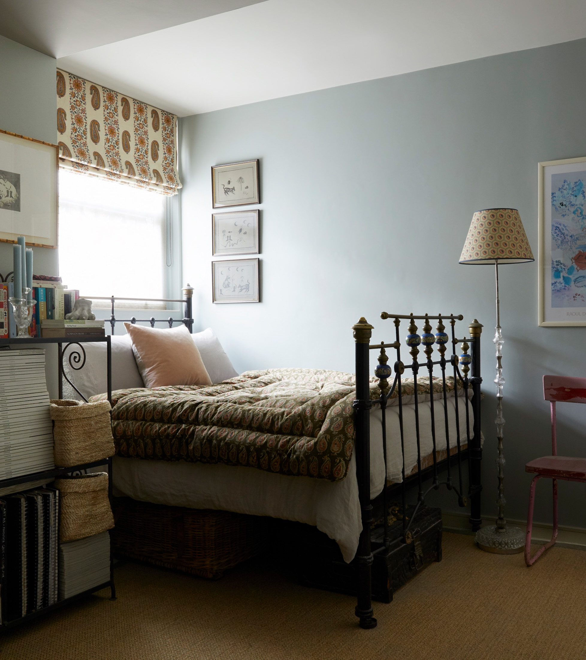 a bedroom with a pale blue wall, an iron double bed in front of a window with an earthy bed spread