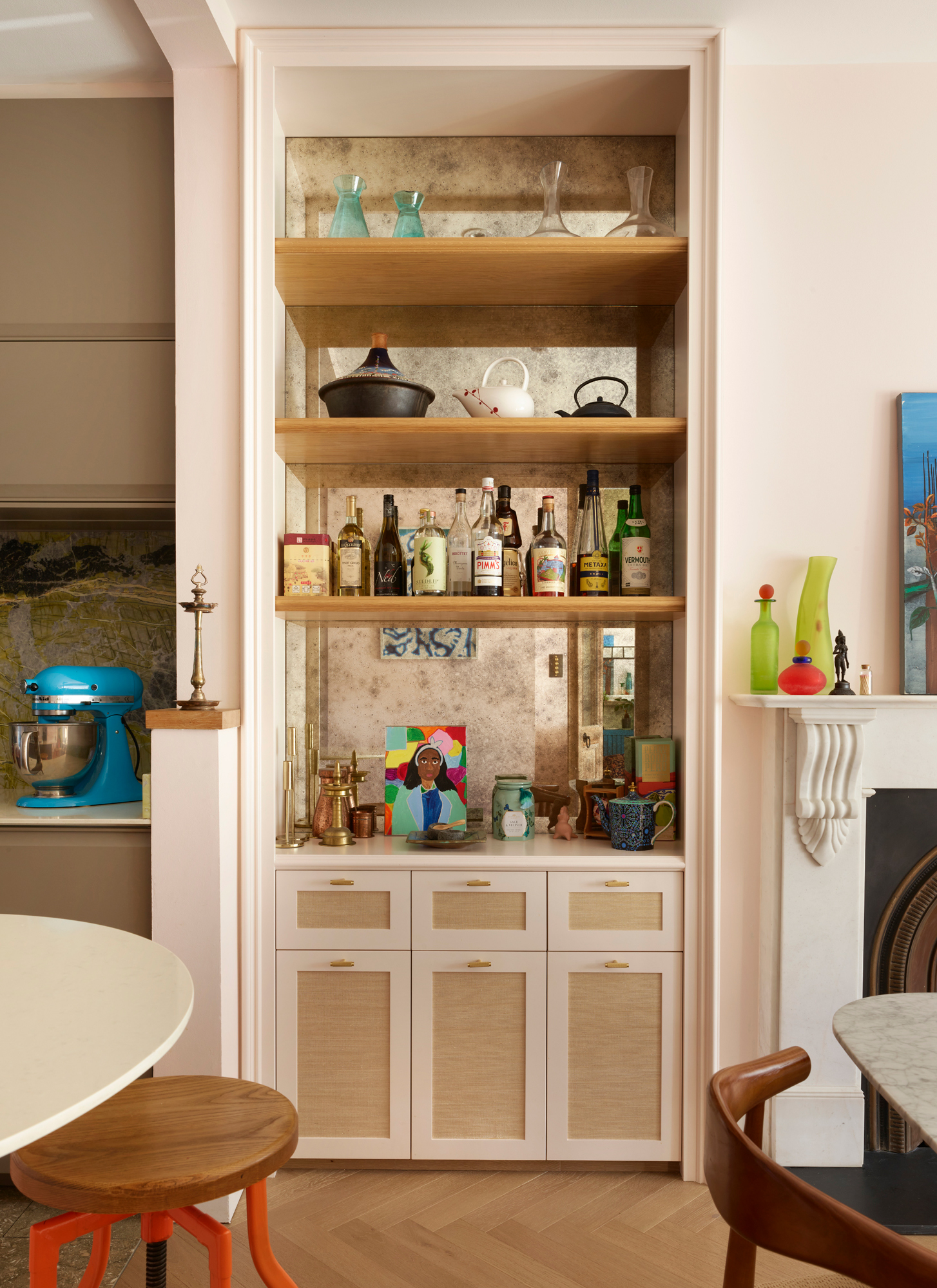 a kitchen pantry bar area with shelving full of bottles and glasses,rattan door fronts, a blue kitchenaid and a white marble fireplace