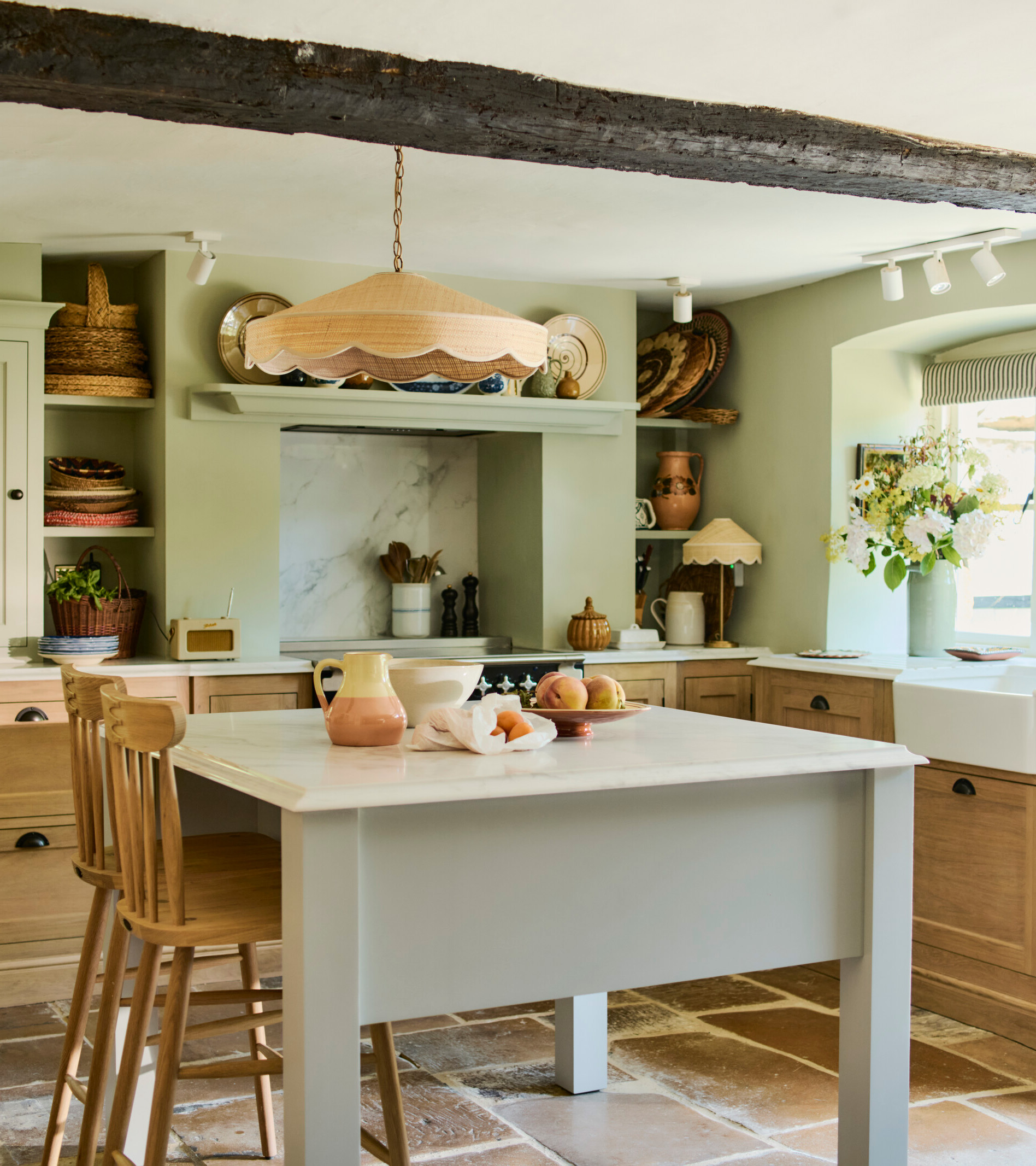 a country kitchen with sage green walls and dark wooden beams, brown wooden cabinetry and a grey kitchen island with a white marble top