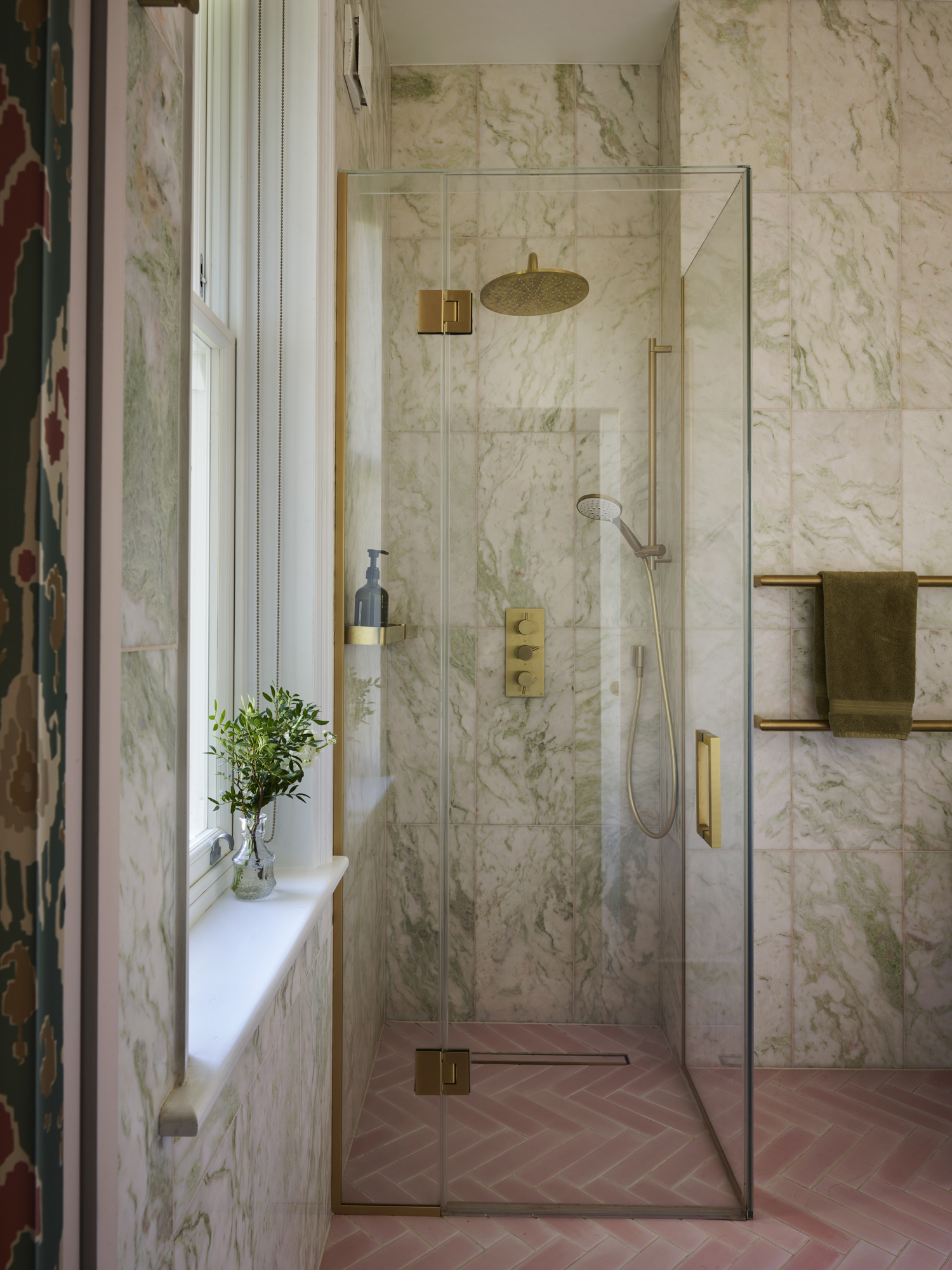 a bathroom pictured with walls lined with marble, a shower with gold hardware is the focal point of the image