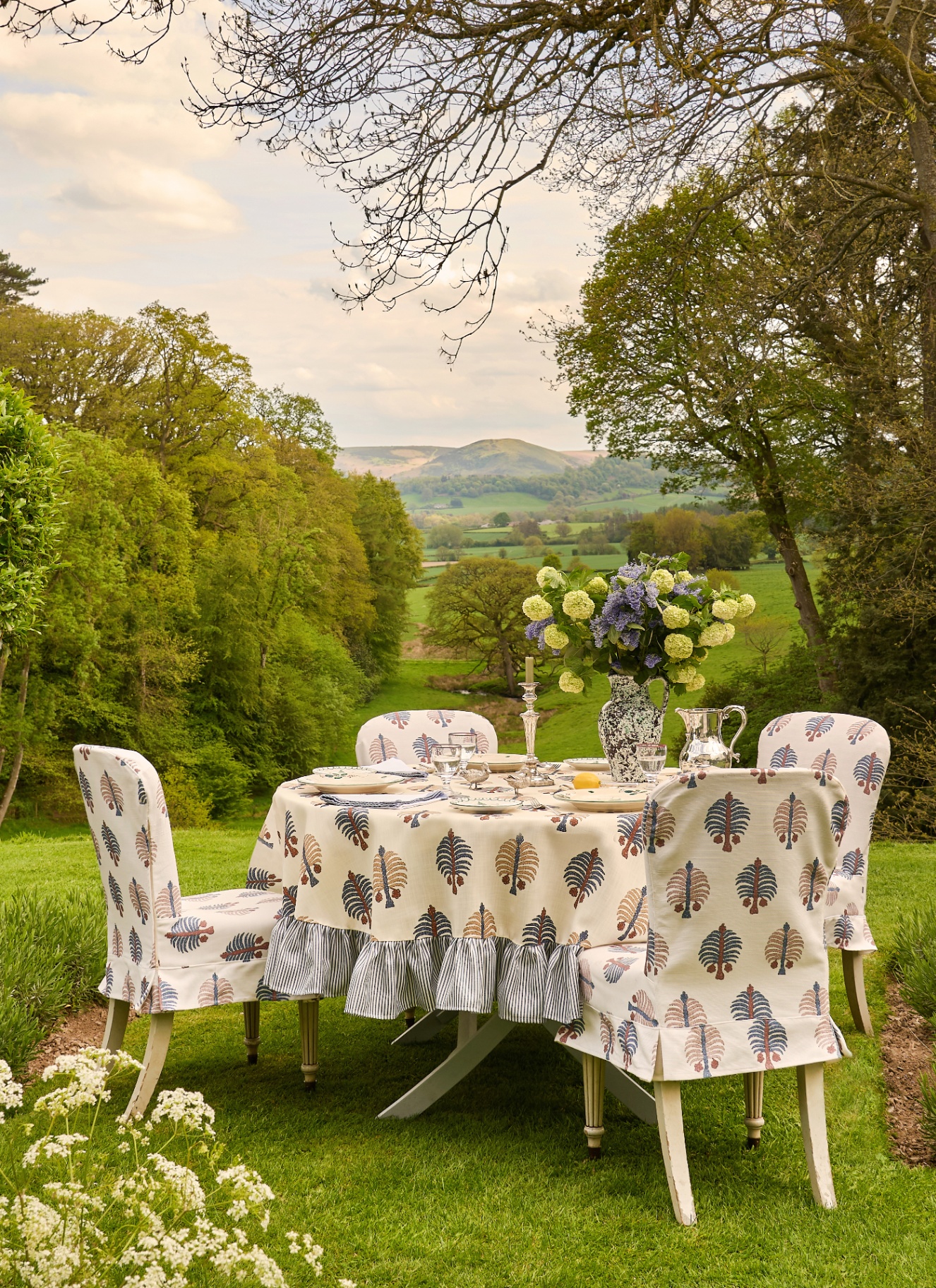 a garden with a round outdoor table and chairs both covered in a white and blue botanical print fabric