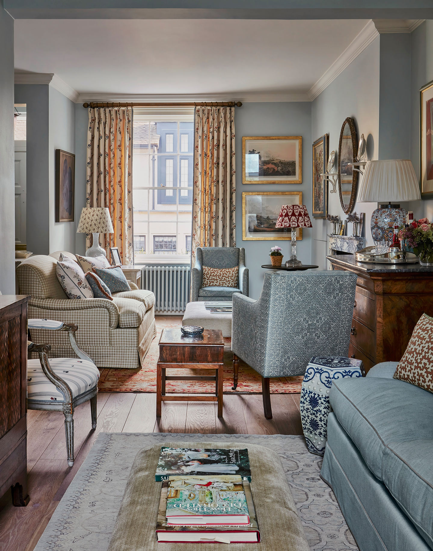 A view through an open-plan drawing room with a blue and white colour scheme. In the background area is a sofa and two armchairs around an ottoman, and in the foreground is a blue sofa and chenille ottoman on a rug