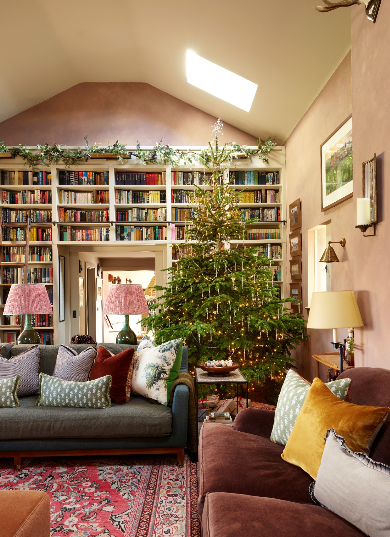 A tall Christmas tree decorated with warm lights standing beside double-height floor-to-ceiling library bookshelves