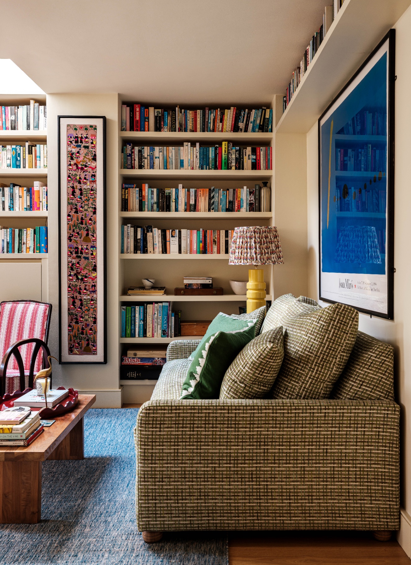 A cozy sitting room featuring high-level floating bookshelves running along the top of the wall, with a textured green sofa, decorative cushions, and framed artwork below