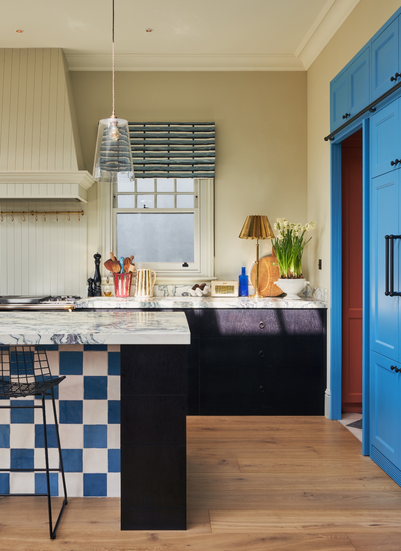 a kitchen with a bright blue door, a kitchen island with white and blue checkerboard tiles, dark blue kitchen cabinetry and beige walls