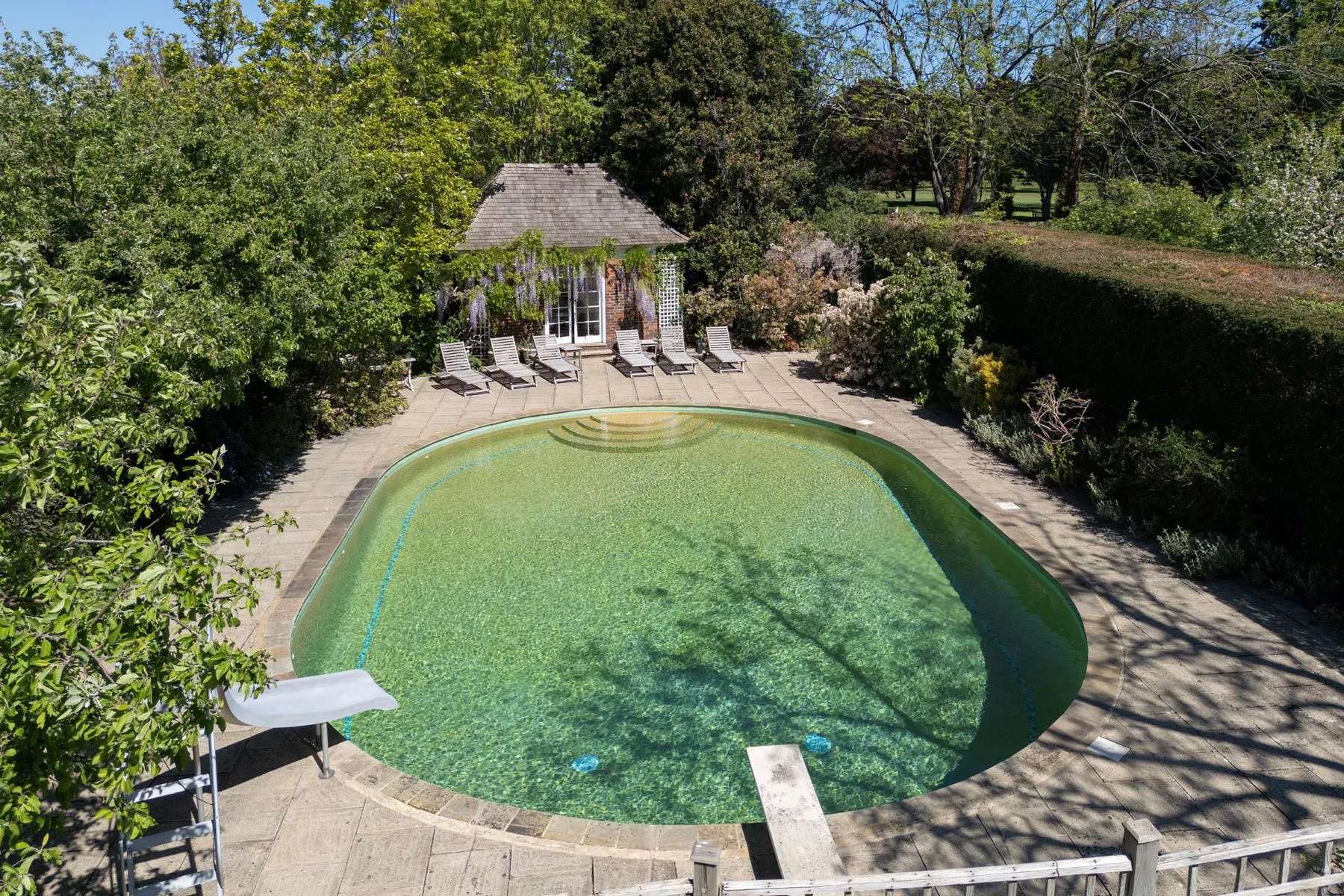 the outdoor pool area of ormeley lodge, with a large pool, poolhouse and sun loungers