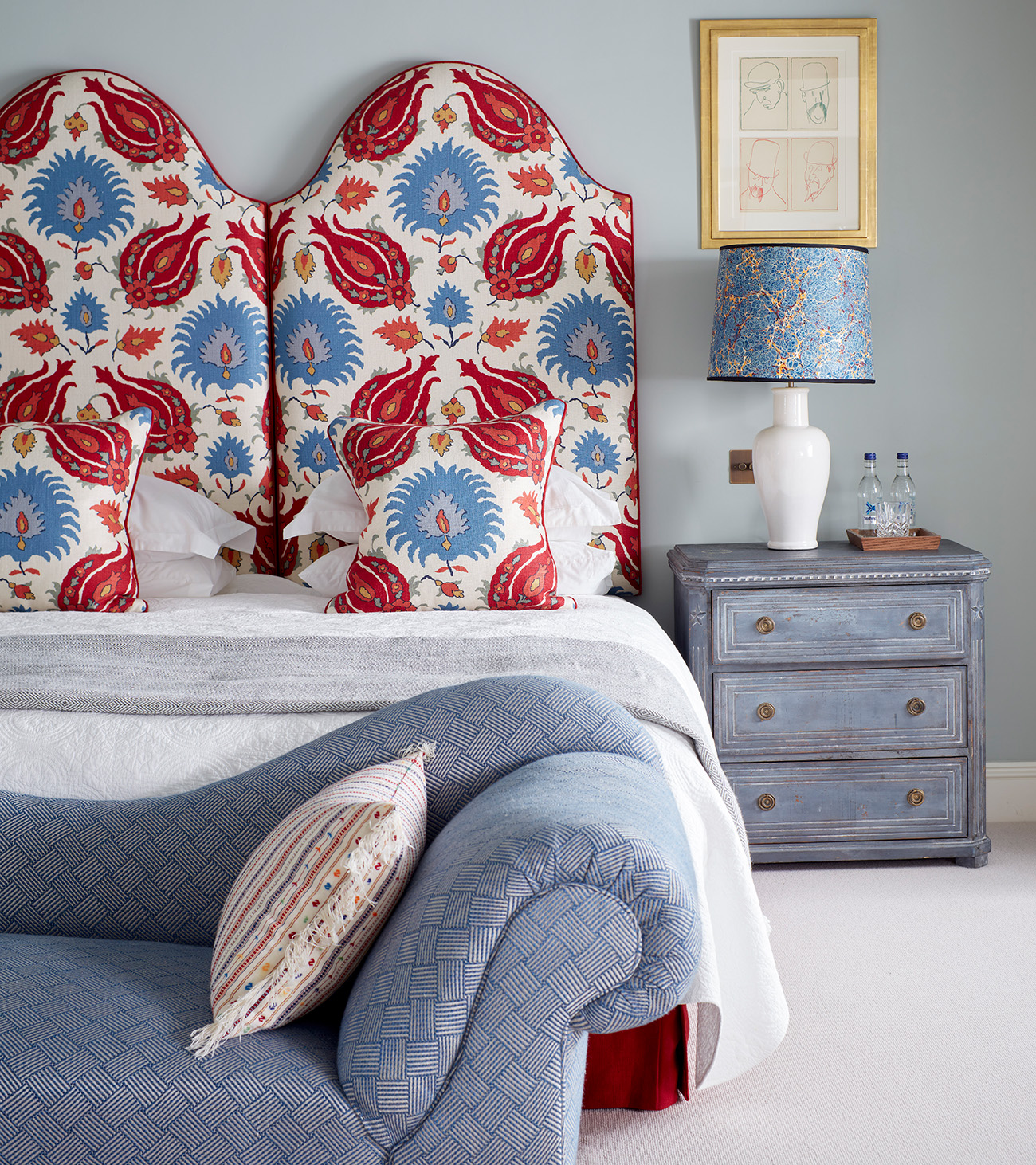 a pale blue bedroom with a double bed with a red patterned headboard