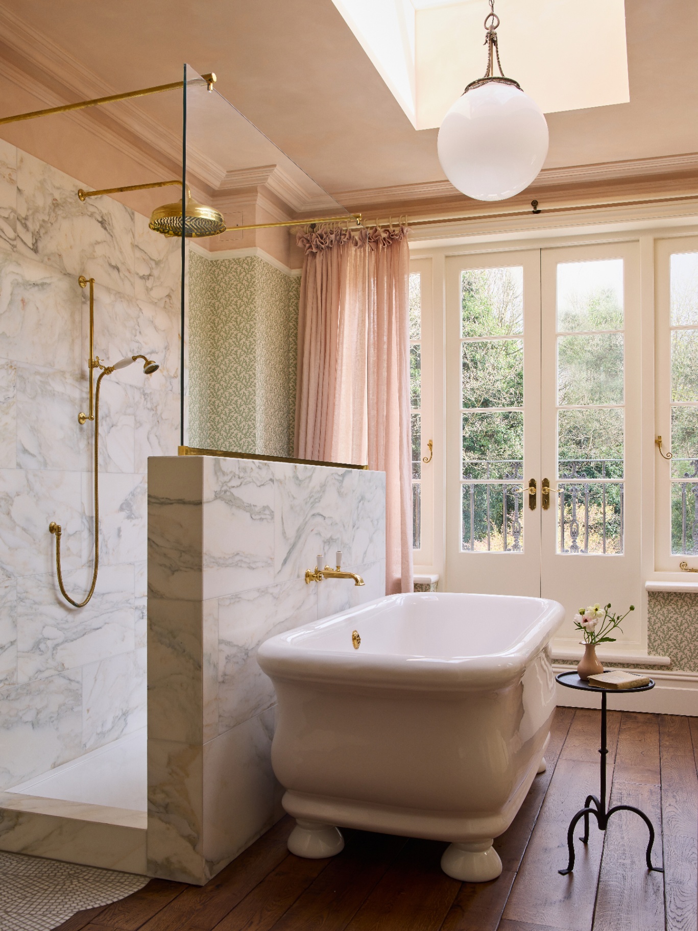 a feminine decorated bathroom pictured with wallpaper wrapping, dusky pink curtains, a roll top bath and a large gold walk in rainfall shower 