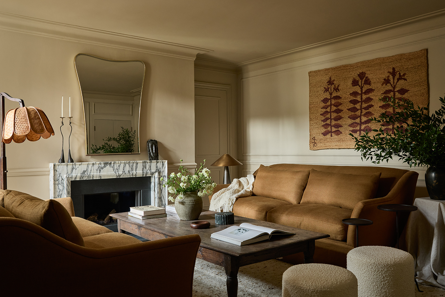 a neutral living room with two mid-brown sofas either side of a vintage wooden coffee table. A marble fireplace is on the left wall and two boucle stools sit to the right. Woven art hangs above the sofa on the back wall