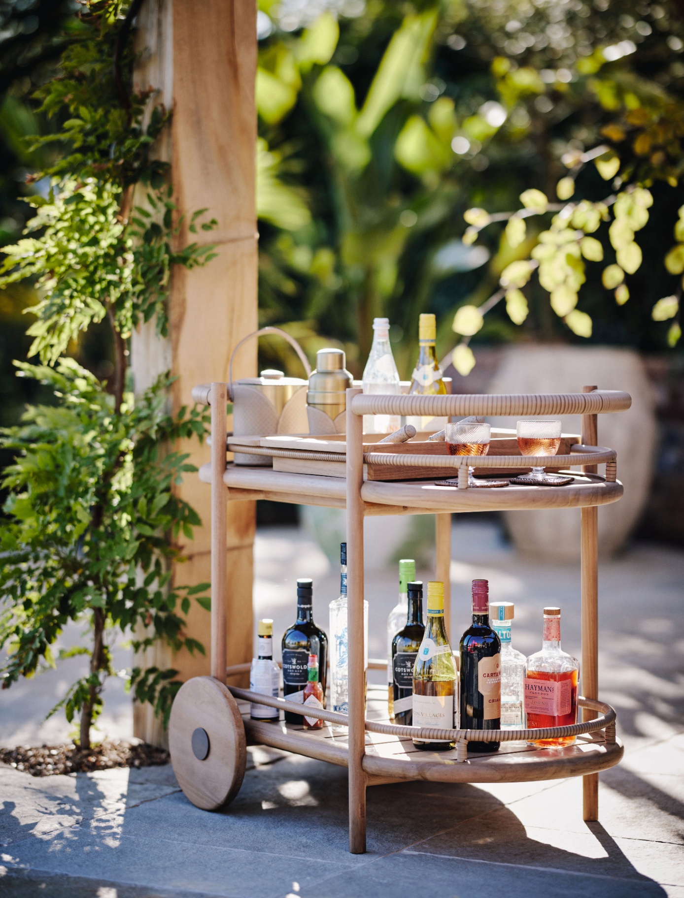 a wooden drinks trolley filled with drinks bottles and glasses on a grey patio