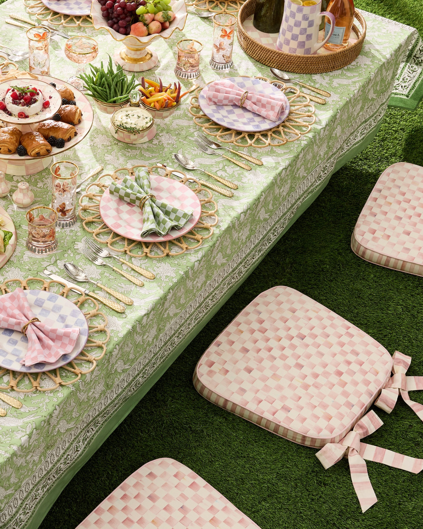 a picnic style spring tablescape with a green tablecloth, picnic food and white and pink checkered floor cushions