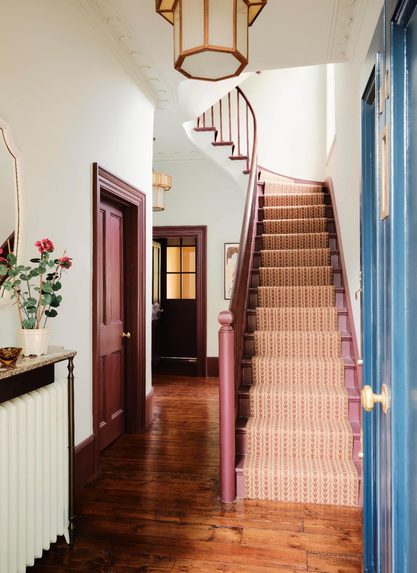 a hallway with wooden flooring, stairs painted in dark red and red and cream patterned runner and red painted doors