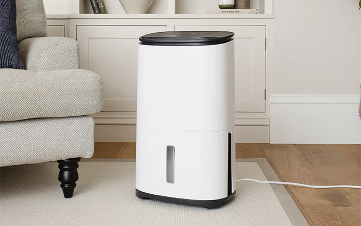 a white and grey dehumidifier on a beige rug on a wooden floor next to a pale sofa