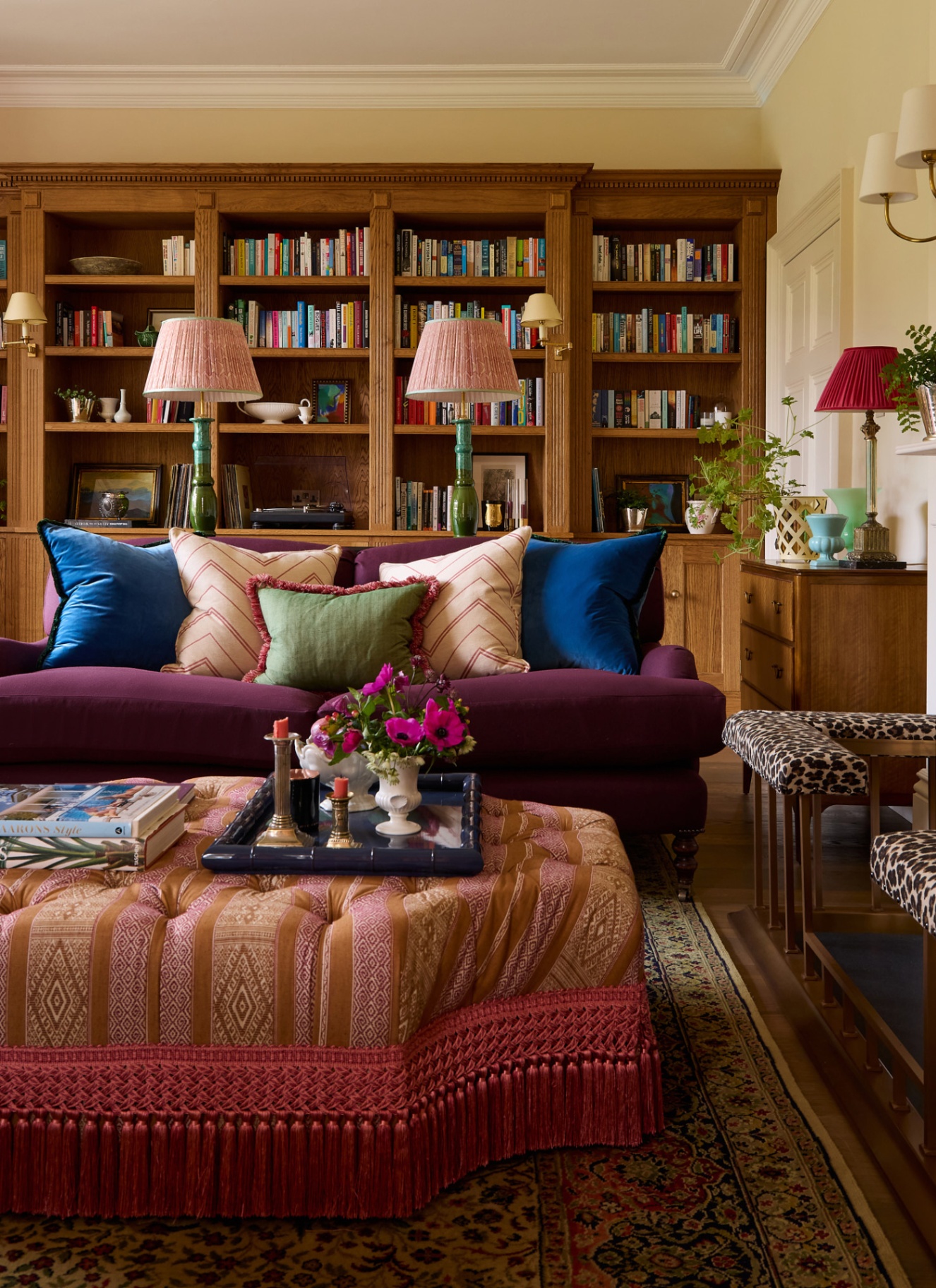 a living room with a purple sofa, a brown and pink upholstered coffee table and a wall covered in a brown wooden bookcase