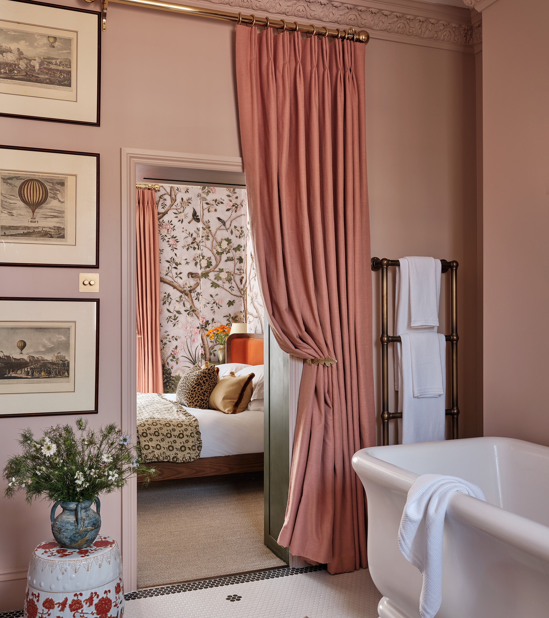 a pink ensuite with a pink curtain as the door looking out on to the bedroom with botanical wallpaper
